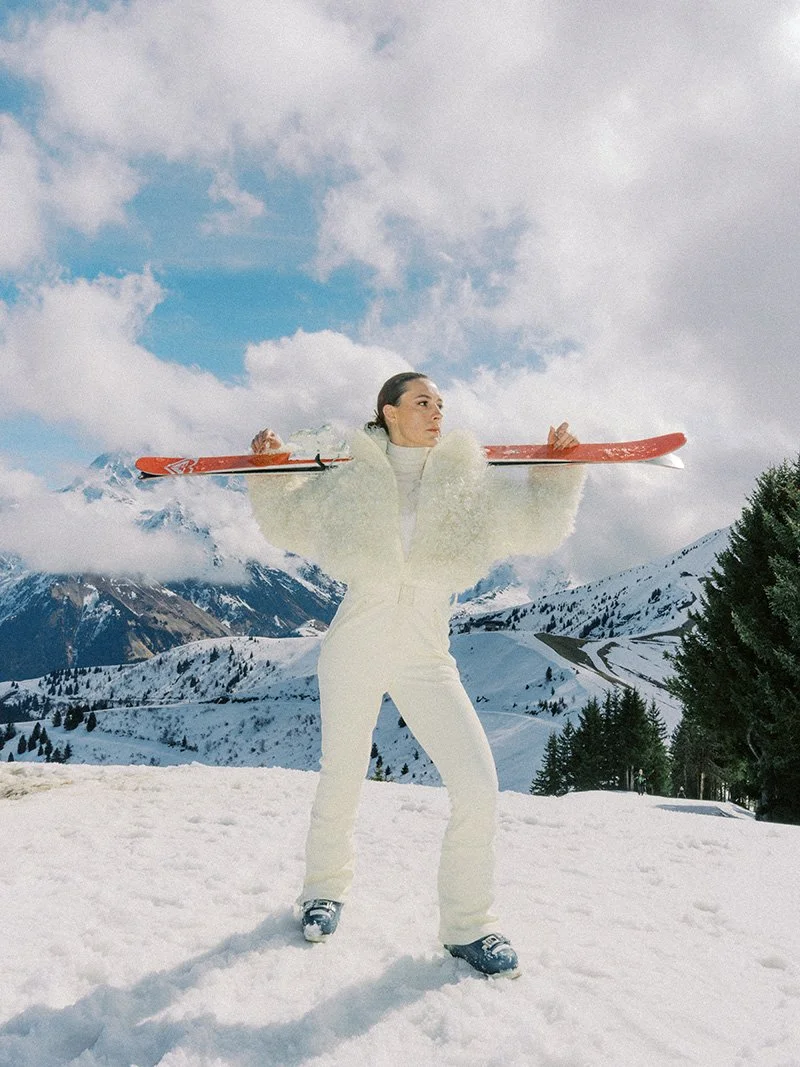 Modern, stunning wedding bride in her cream coloured snow suit with her skis over her shoulders for her wedding celebration in Saint Gervais double border