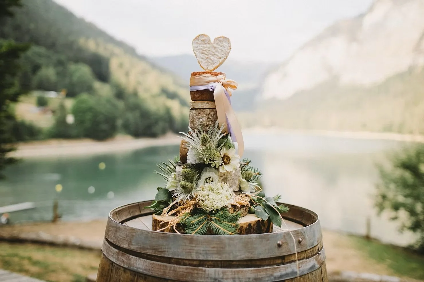 A tiered cheese cake with a heart made of cheese on top, with a background of Lake Montriond