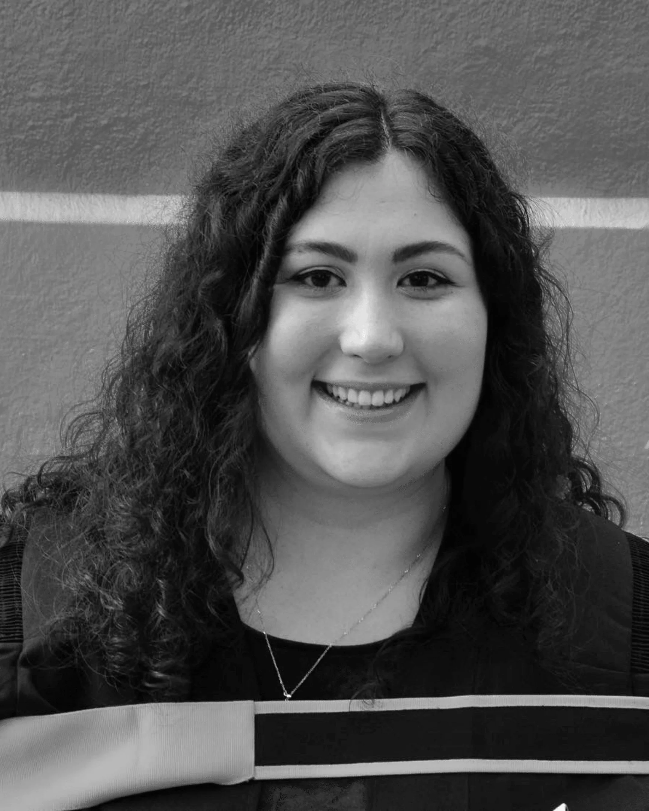 Black and white photo of a person smiling with long, curly hair wearing a graduation gown.