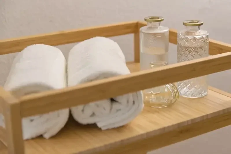 Ein Holztablett mit zwei weißen Handtüchern, vier Glasflaschen mit Wasser oder Duftöl, auf einer Holzoberfläche.