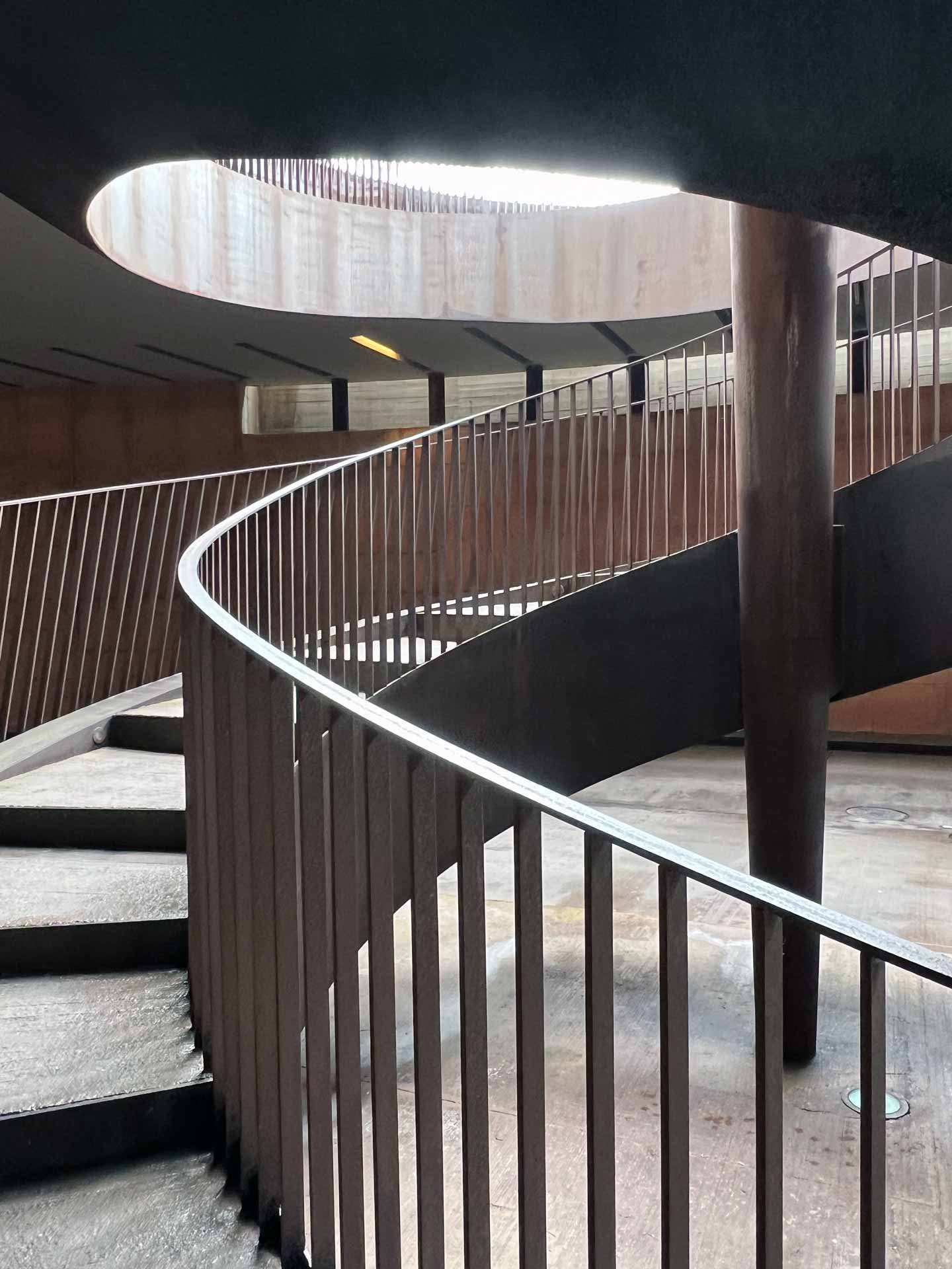 Innenaufnahme eines modernen spiralförmigen Treppens mit Holz- und Metallmaterialien, Lichtquelle von oben.