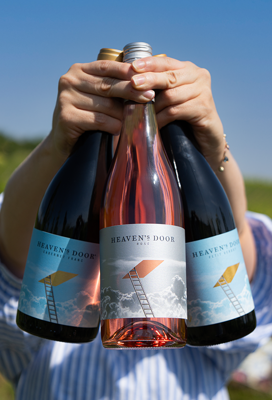 Person hält drei Flaschen Rosé-Sekt im Freien