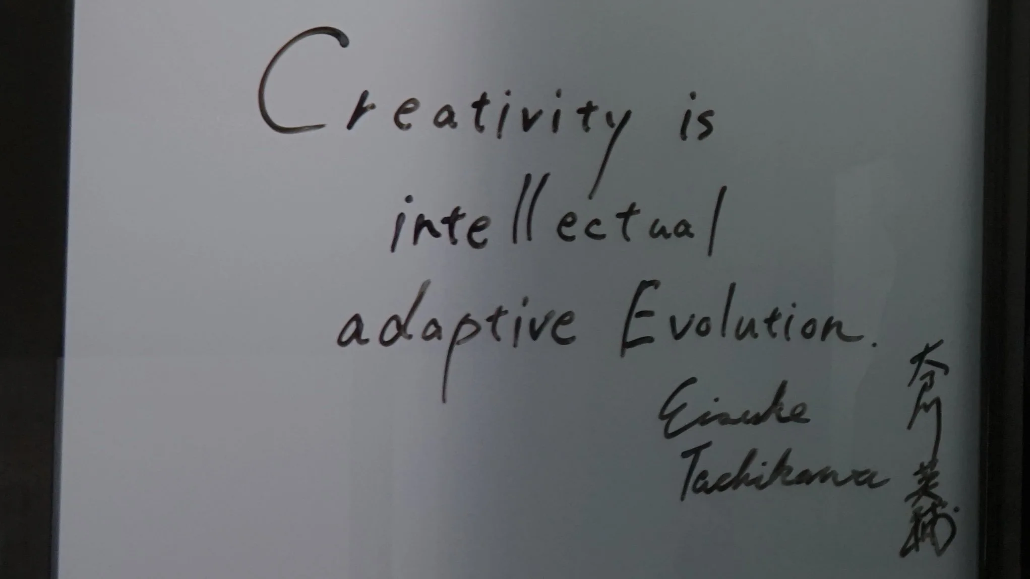 Handwritten note by Eisuke Tachikawa on glass reading “Creativity is intellectual adaptive evolution,” with his signature in English and Japanese Kanji on the right.