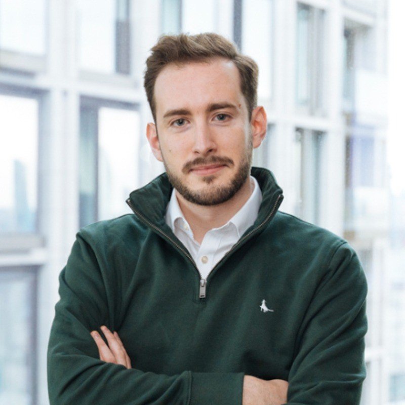 A woman with curly dark hair, glasses, earrings, and a striped top smiling indoors.
