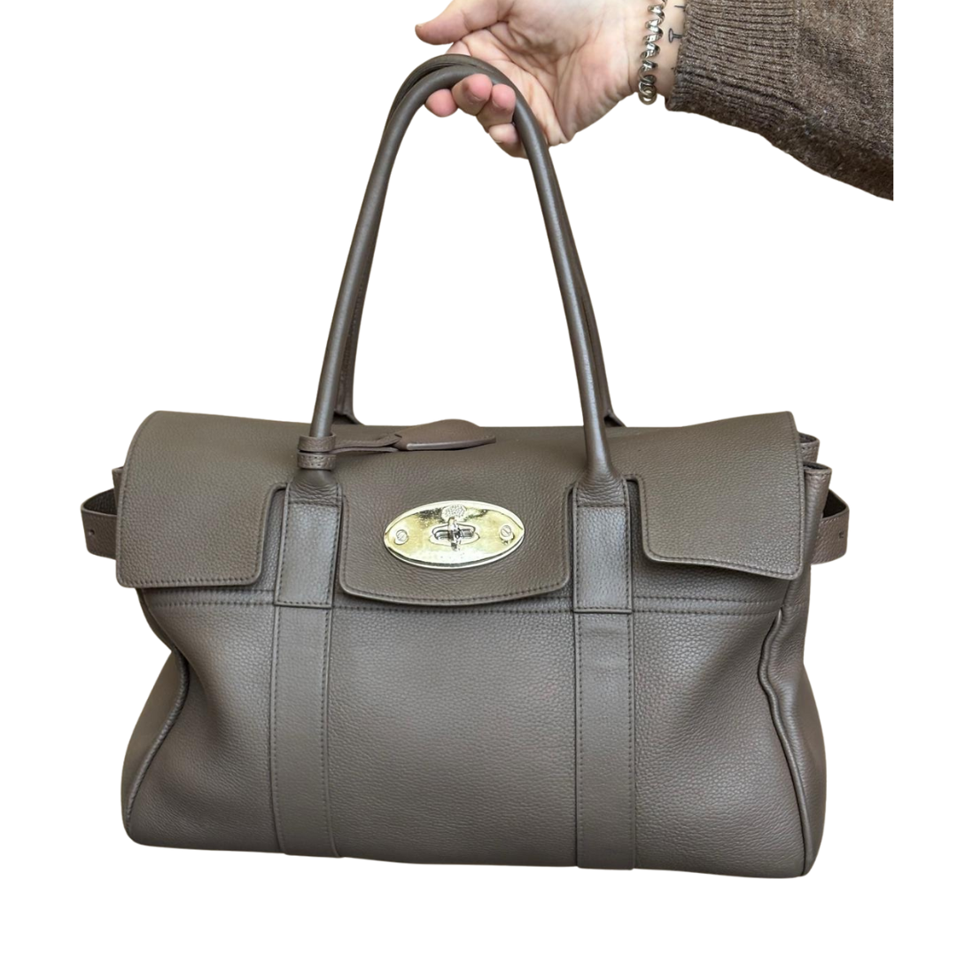 Hand hält eine graue Lederhandtasche mit goldener Schlossverschluss gegen weißen Hintergrund.