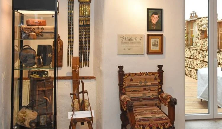 Das Winklmayr Museum mit antiken Möbeln, einem Glasvitrinenkasten, einer Holzsitzecke, einem Wandschrank mit Fotos und Kunstwerken, Zugang zu einer Terrasse im Freien.