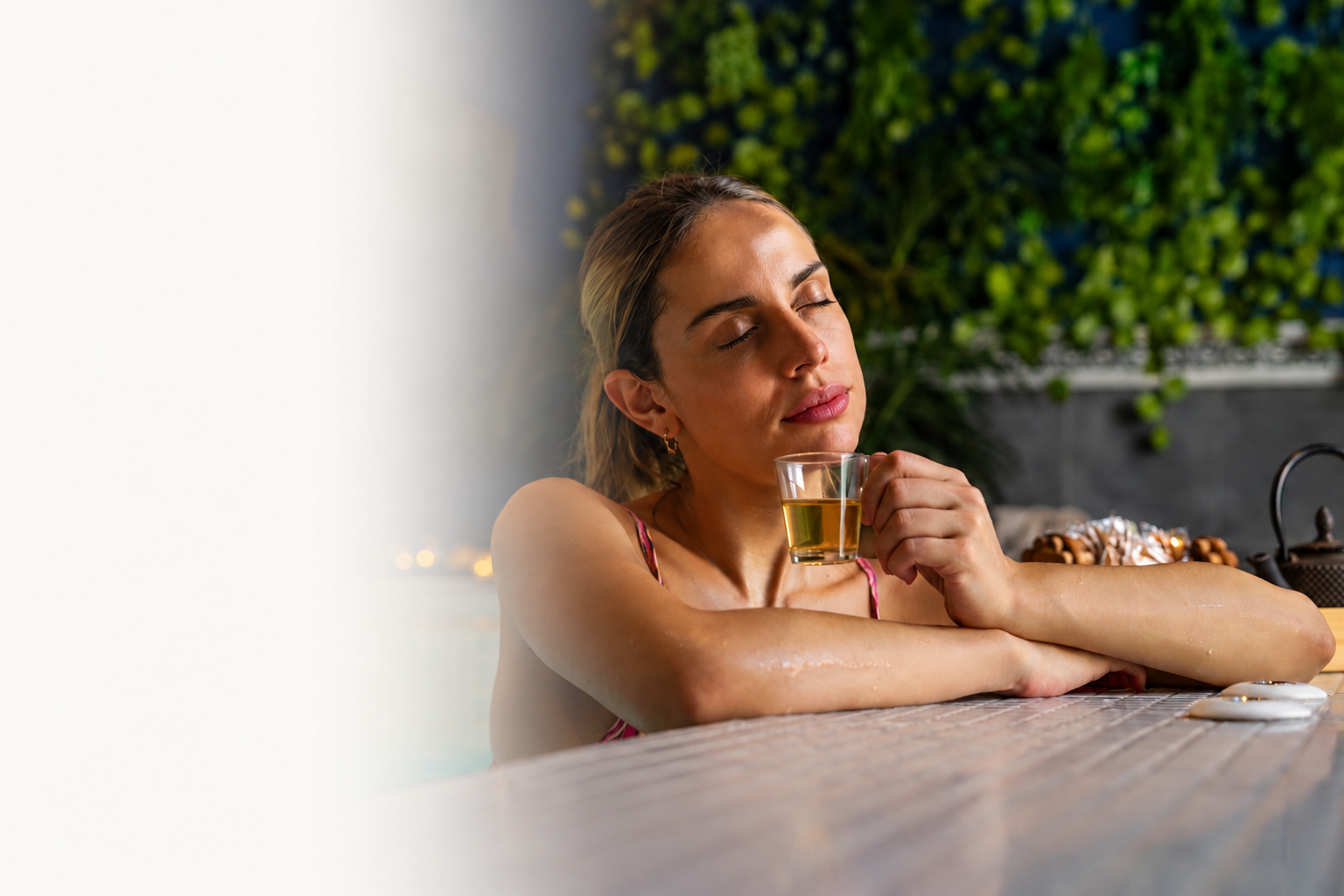 Mujer disfrutando un baño relajante con una taza de té en un ambiente tranquilo y rodeada de vegetación.