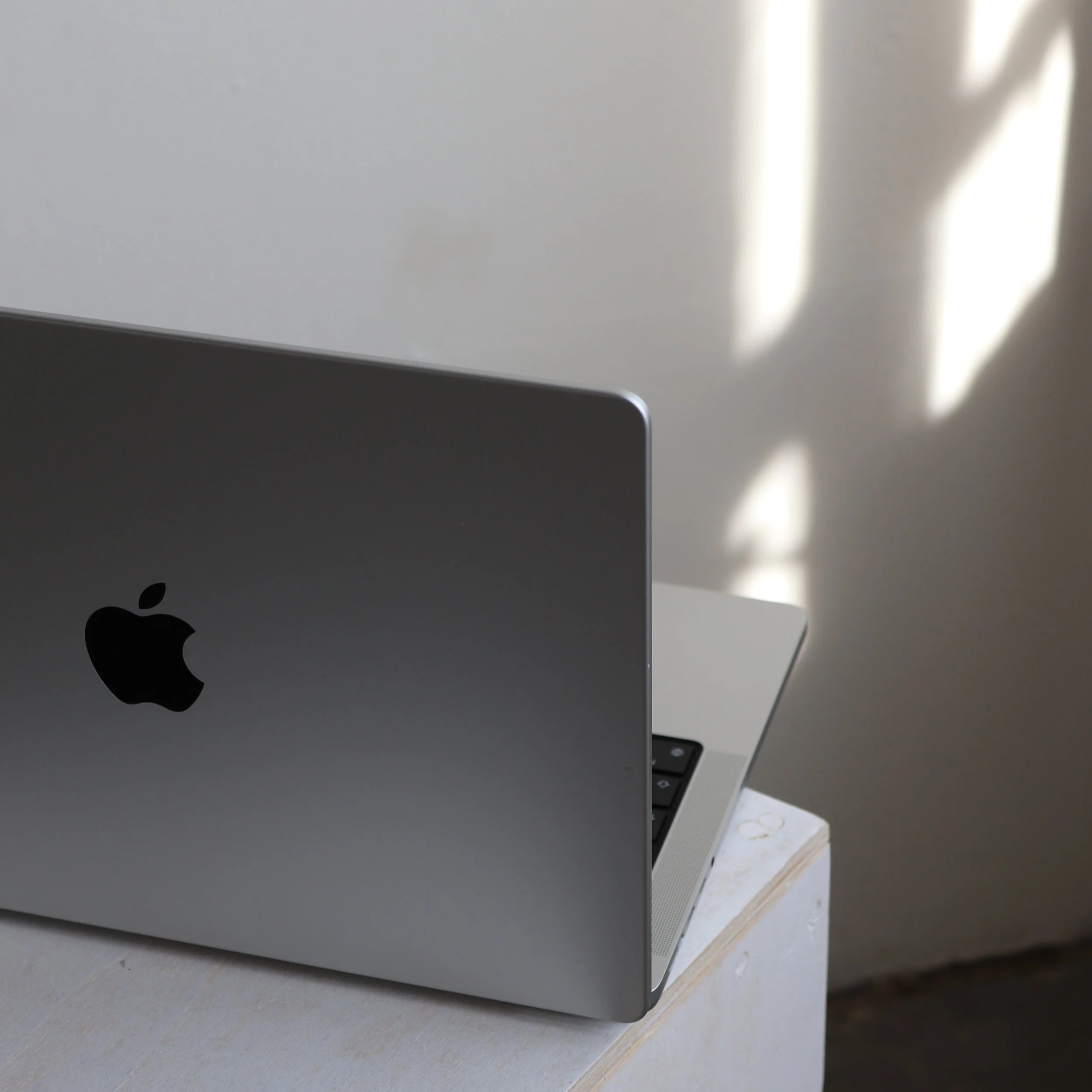 Silberner MacBook auf einem weißen Tisch, mit Schatten einer Pflanze an der Wand im Hintergrund.