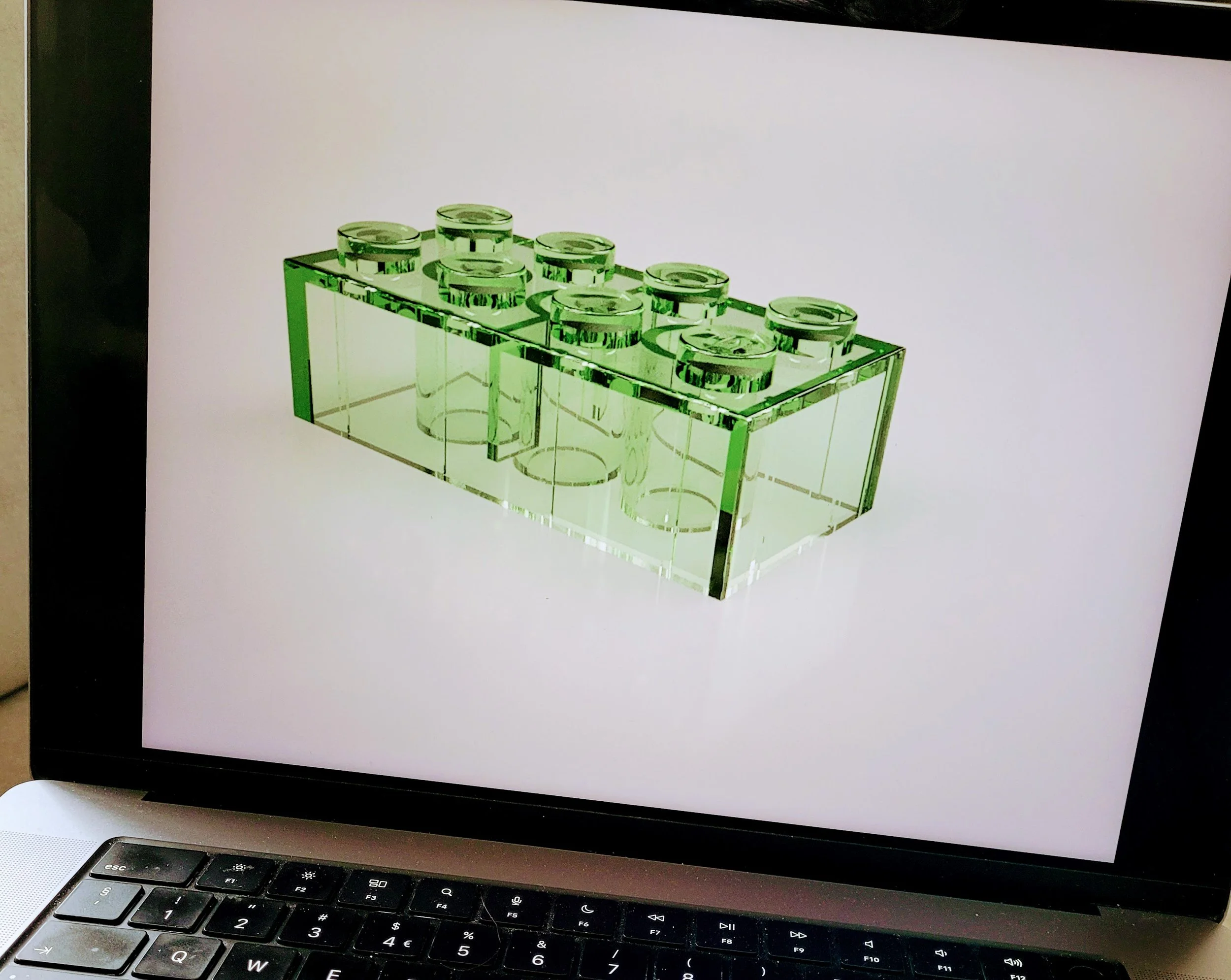 A green translucent brick-shaped object with six circular studs on top, resembling a large LEGO brick, displayed on a laptop screen.