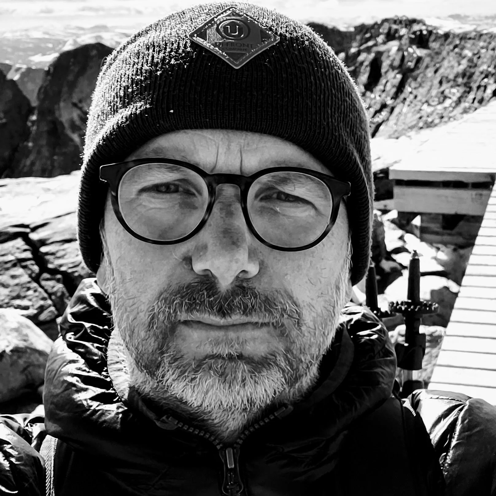 Man wearing glasses and a beanie in a mountainous outdoor setting