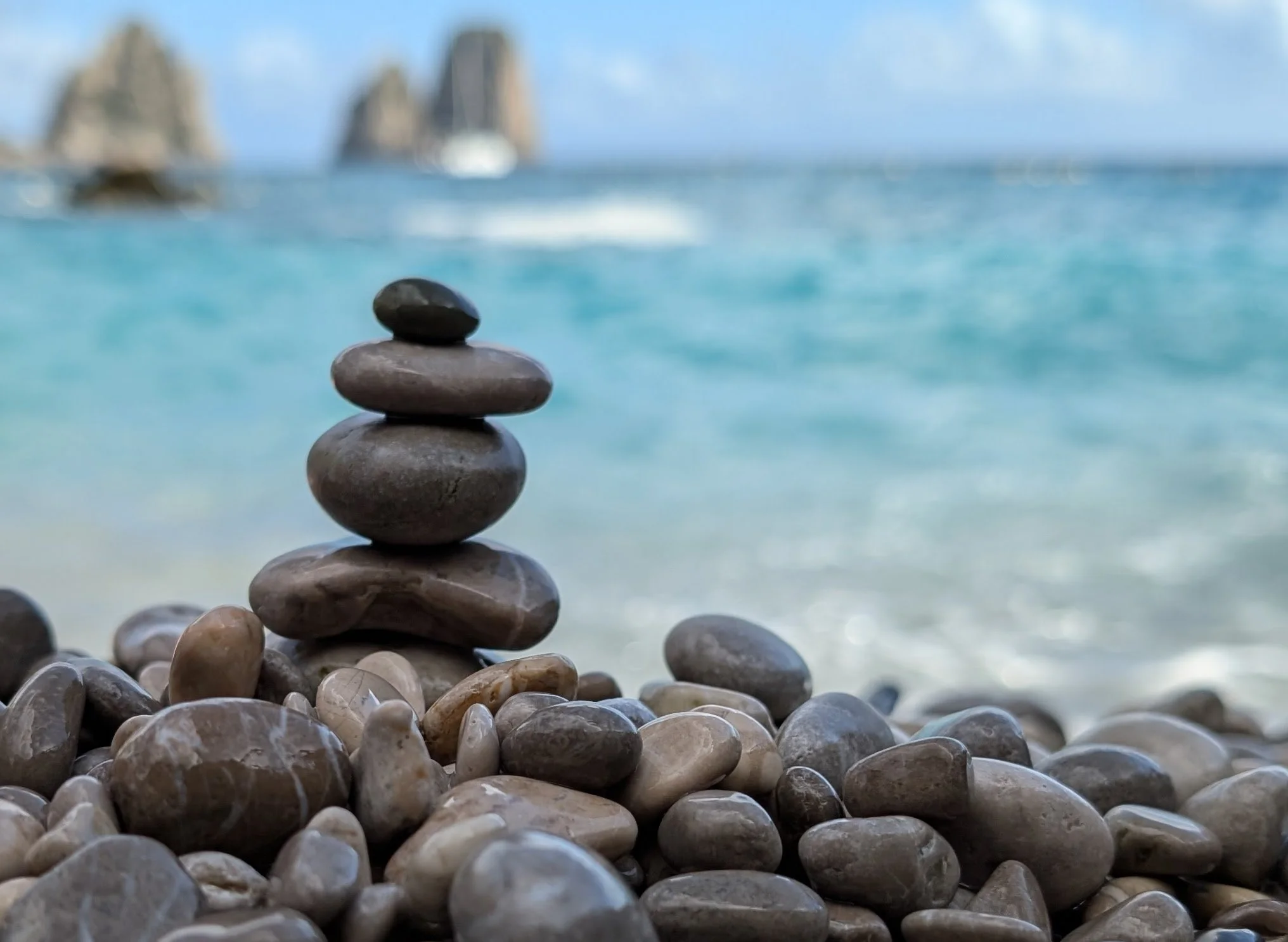 Stack of smooth stones on a rocky beach with blurred ocean background.