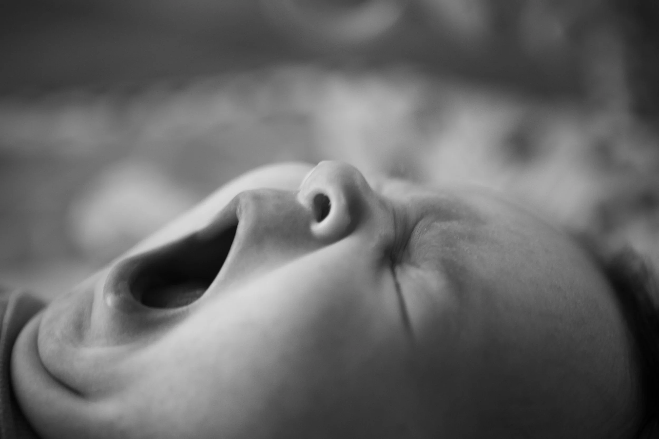 Close-up of a yawning baby in black and white.