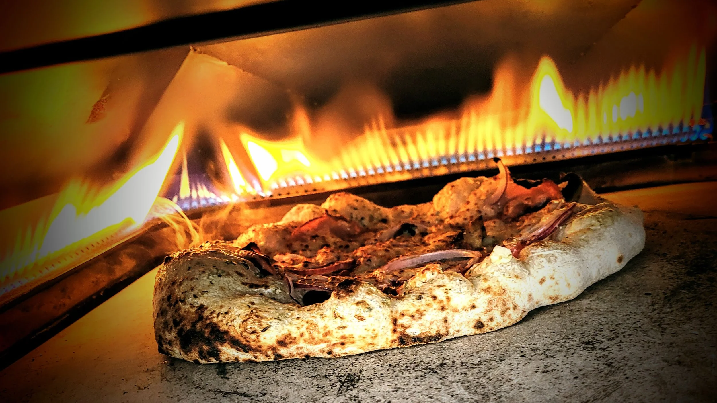 Wood-fired pizza cooking in an oven with visible flames.