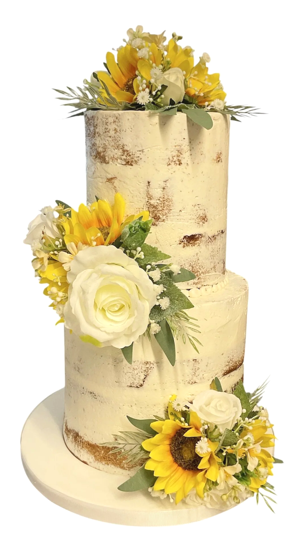 A two-tier white wedding cake with a rustic finish, decorated with white roses, sunflowers, and green foliage.