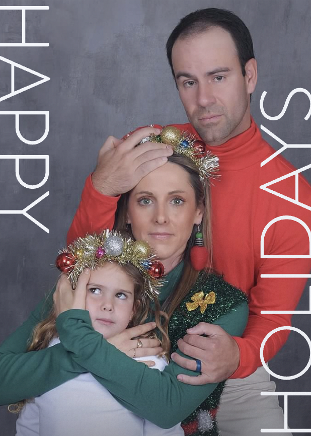 A family holiday photo with a man, woman, and child wearing festive attire and decorations. The text "Happy Holidays" is written vertically on the left and right sides.