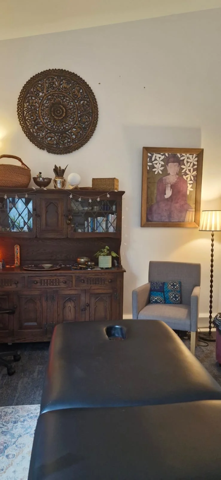 Living room with a wooden cabinet, framed portrait, armchair, tall floor lamp, and decorative wall art.