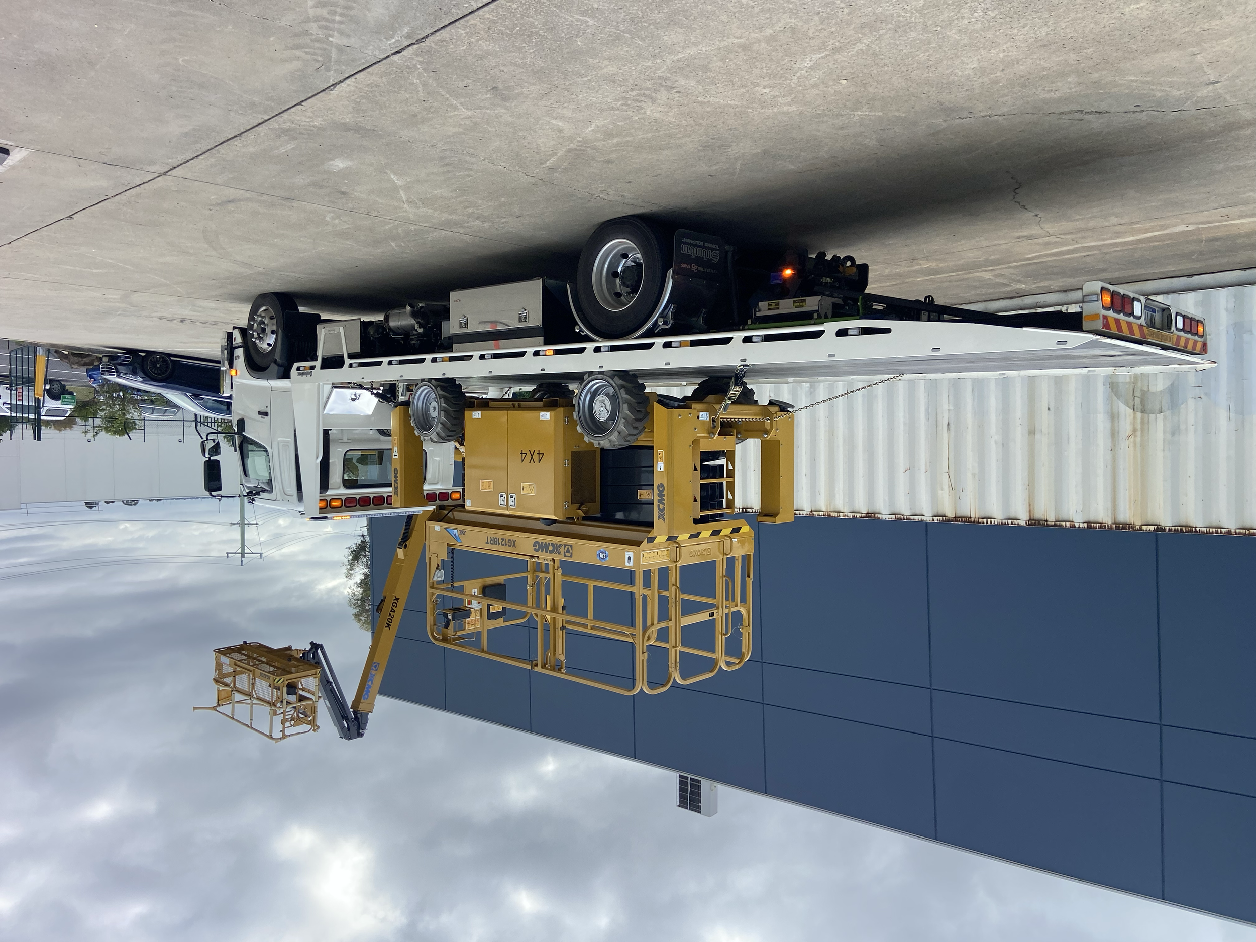 Flatbed tow truck with a large yellow scissor lift parked on a concrete surface.