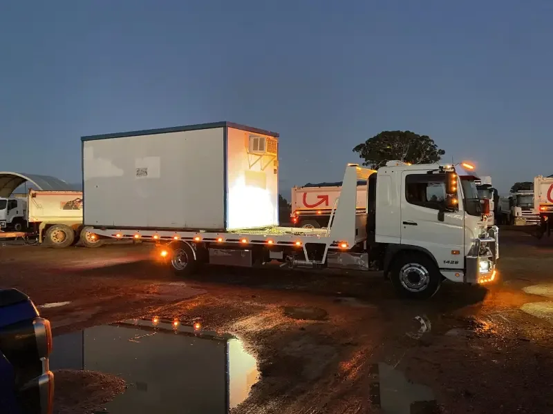 Flatbed truck transporting large white container at dusk