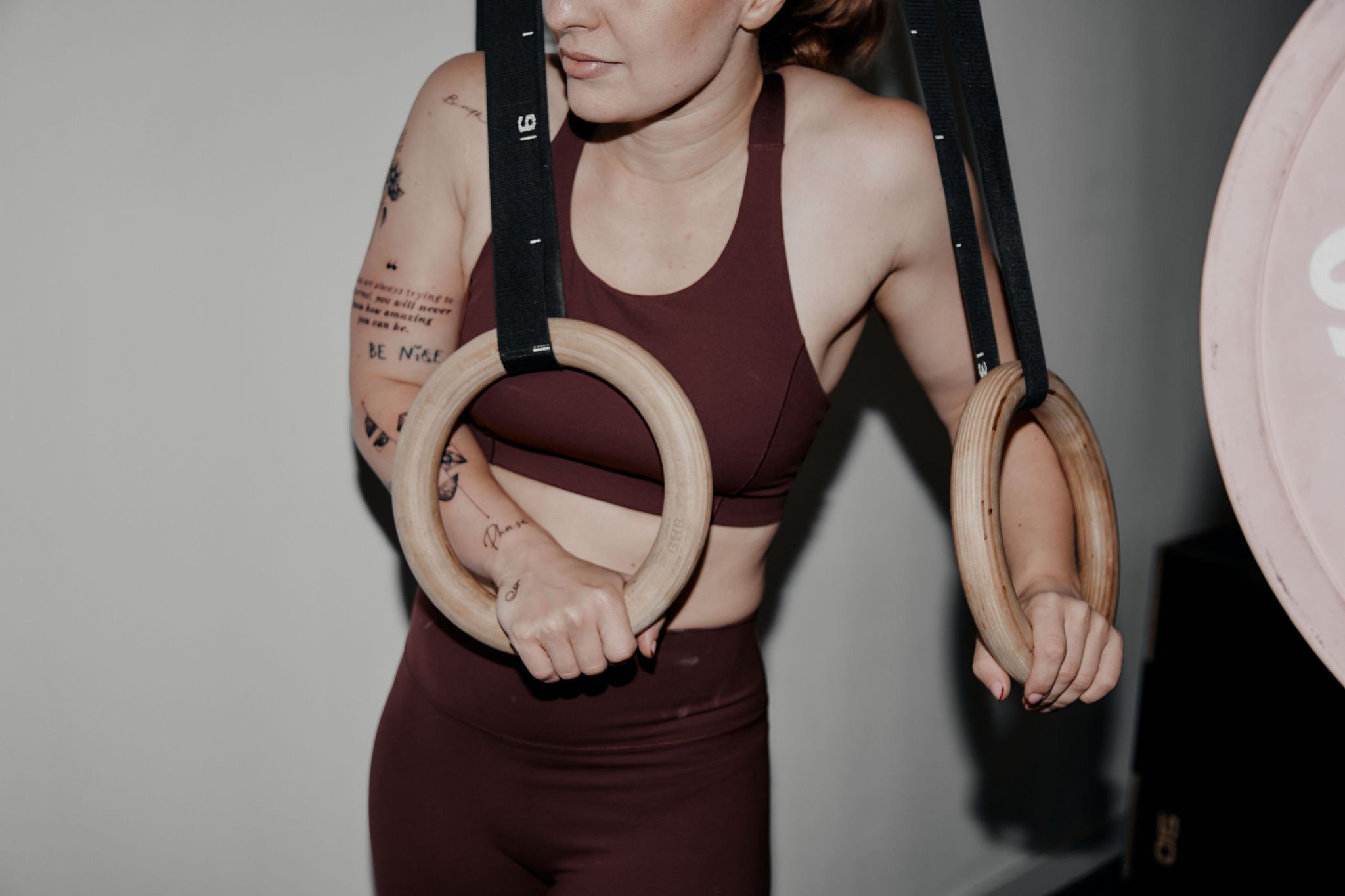 Frau trainiert an einem Horizontalstangentraining mit Turnringen, trägt Sport-Bra und hat Tattoos auf Armen.