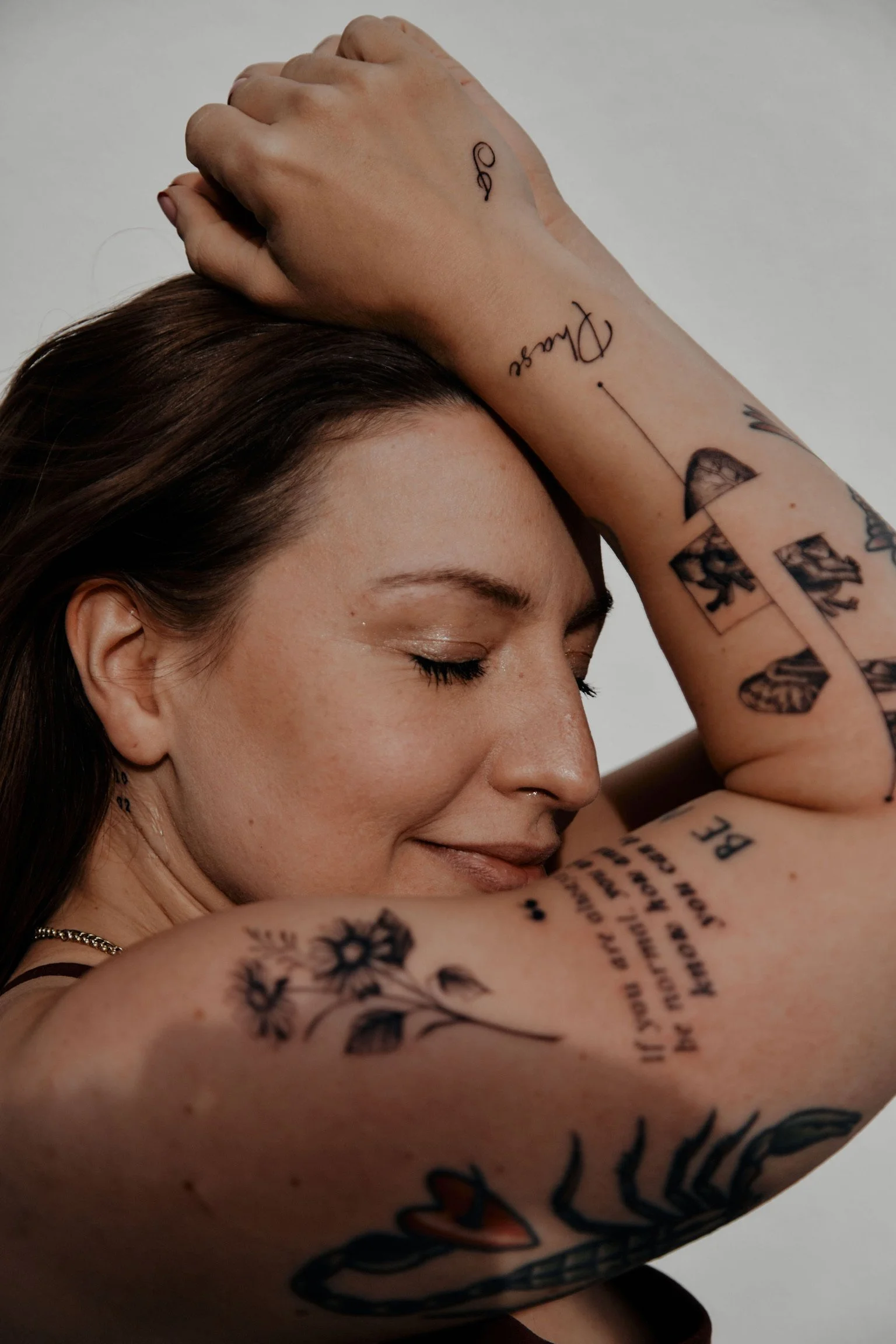 Nahaufnahme eines lachenden Mädchens mit tätowierten Armen, das die Augen geschlossen hat, mit einem hellen, neutralen Hintergrund.