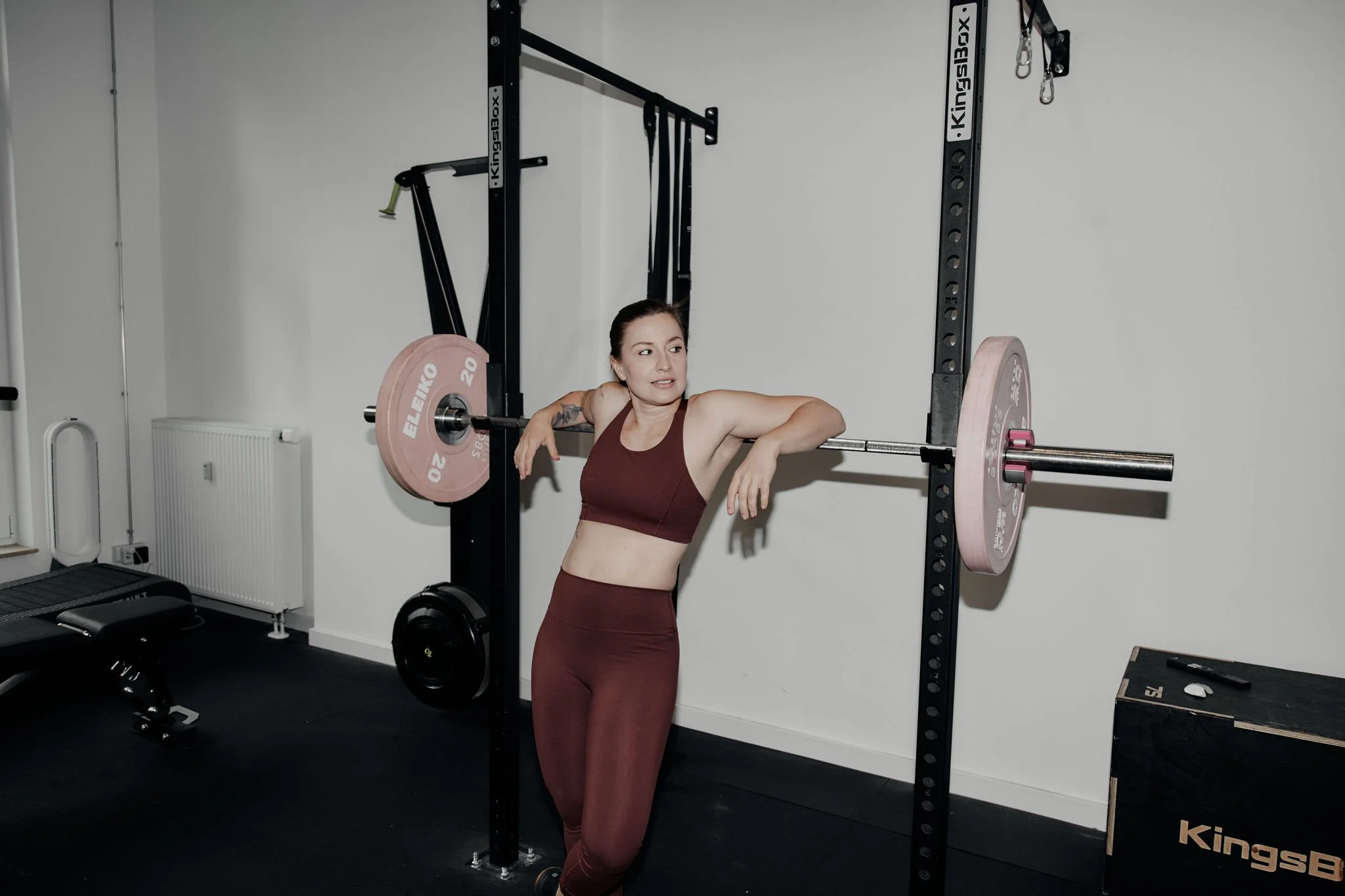 Frau in Sportkleidung lehnt an einer Hantelstange in einem Fitnessstudio.