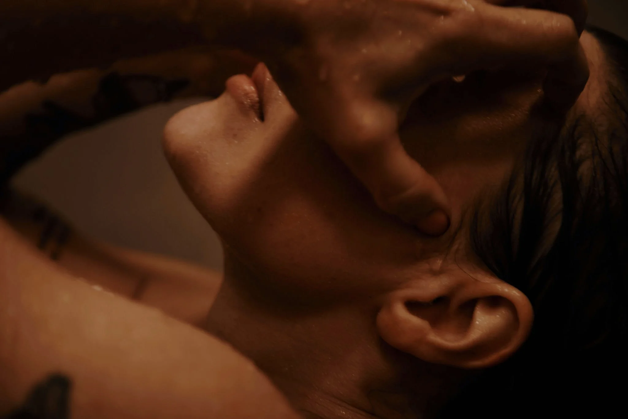 Nahaufnahme von zwei Menschen, die eng aneinanderliegen, mit einer Hand, die eine Person am Kopf hält, bei einer intimen Situation.