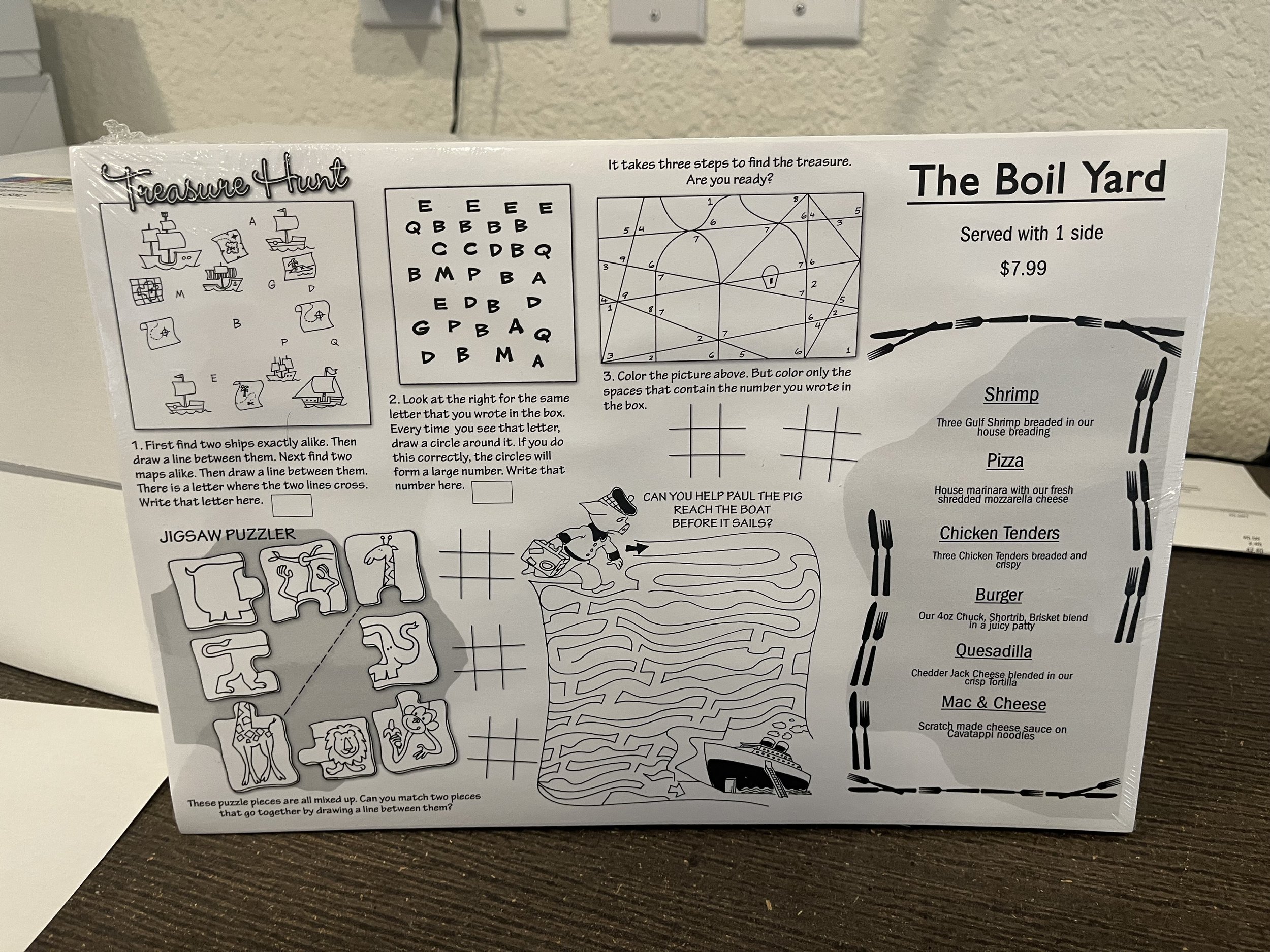 A paper menu with various puzzles and game activities, including a treasure hunt, jigsaw puzzle, and a maze, along with a food menu for a place called The Boil Yard.