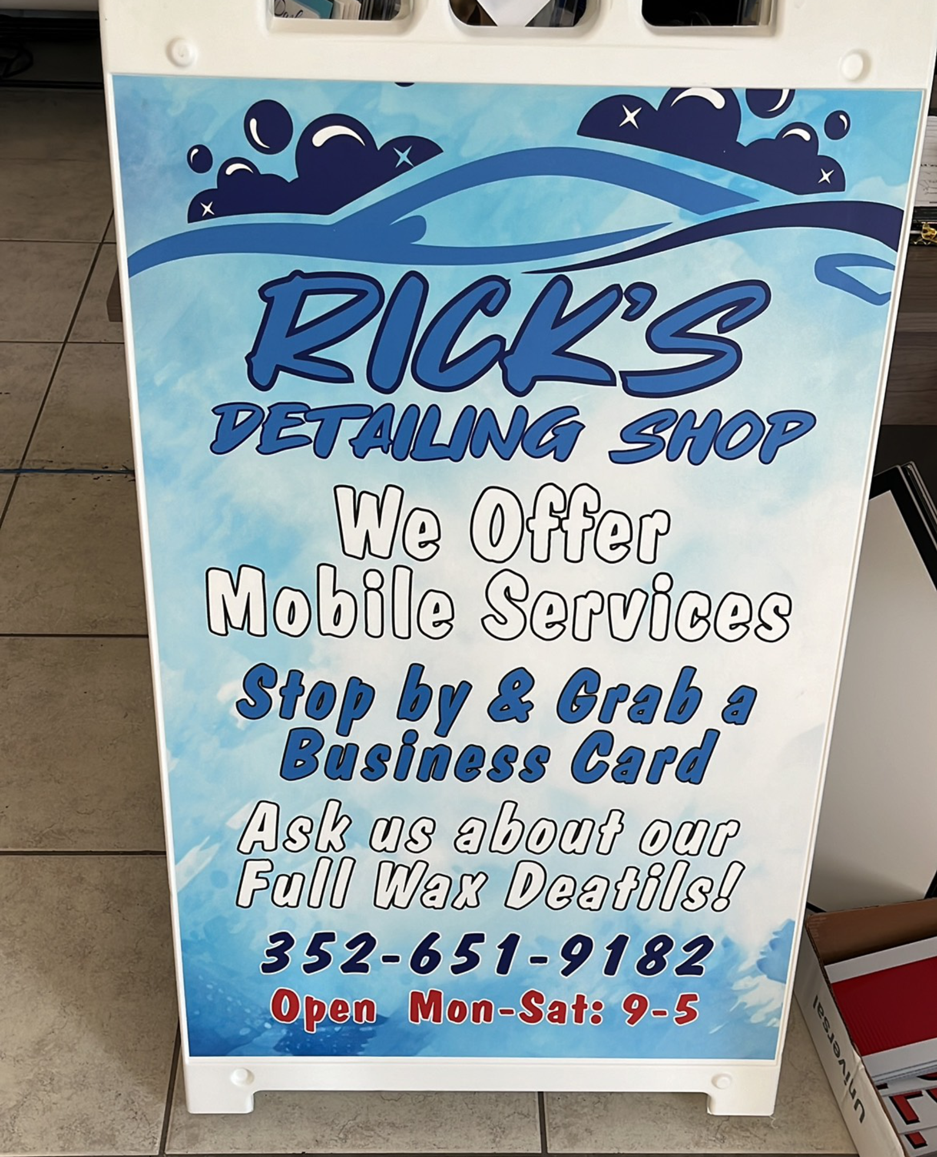 Signboard for Rick's Detailing Shop advertising mobile services, business card grab, full wax details, phone number 352-651-9182, open Monday to Saturday 9 to 5.