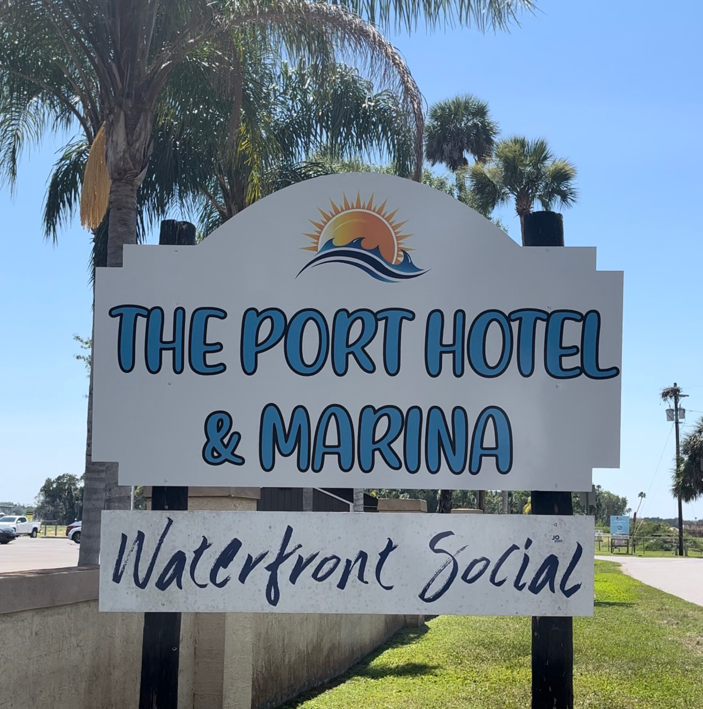 Signboard for The Port Hotel & Marina and Waterfront Social, with a background of palm trees and a clear blue sky.