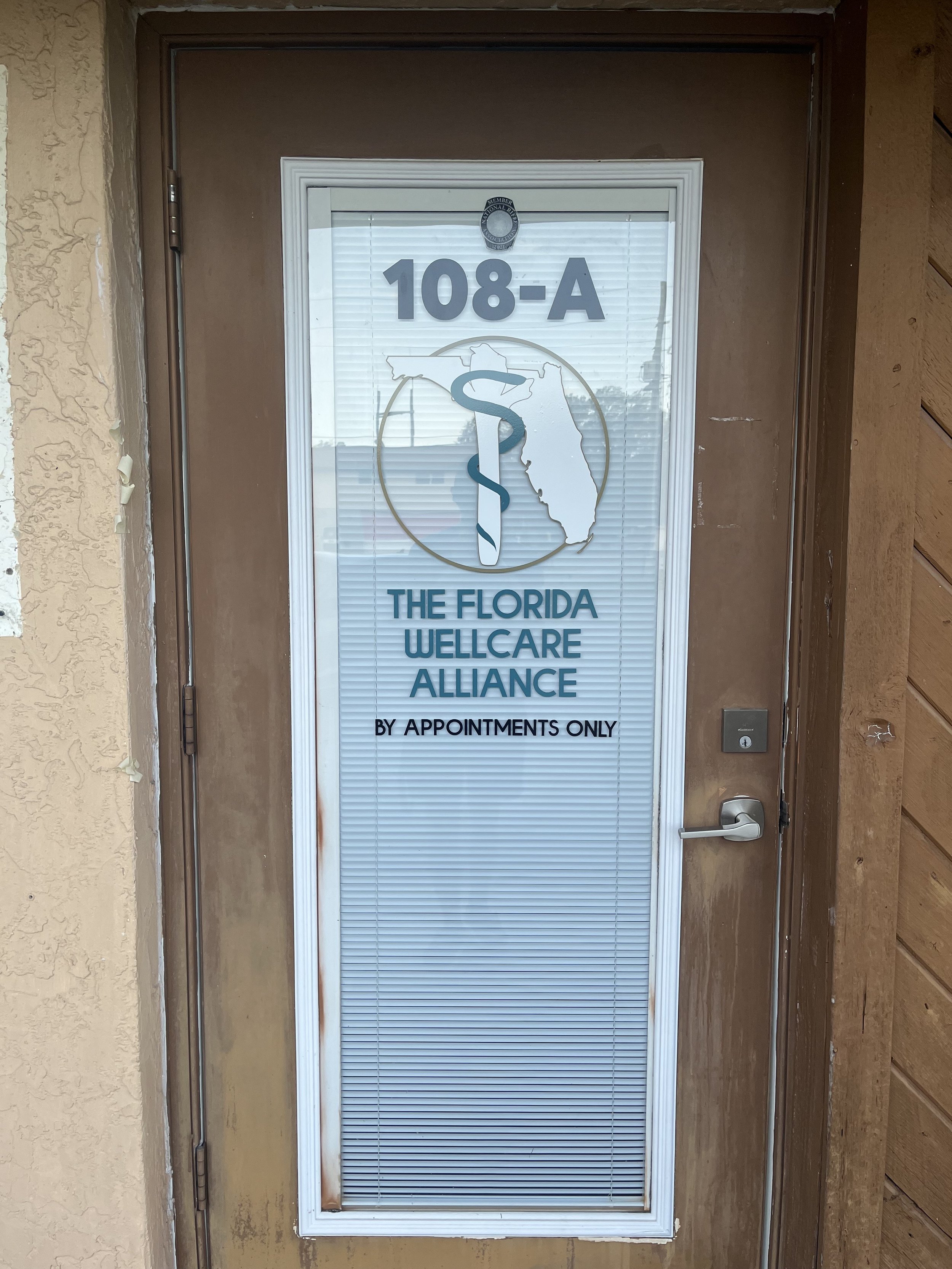Front door of The Florida Wellcare Alliance office with the address 108-A, logo featuring a snake wrapped around a rod, and text indicating appointments only.