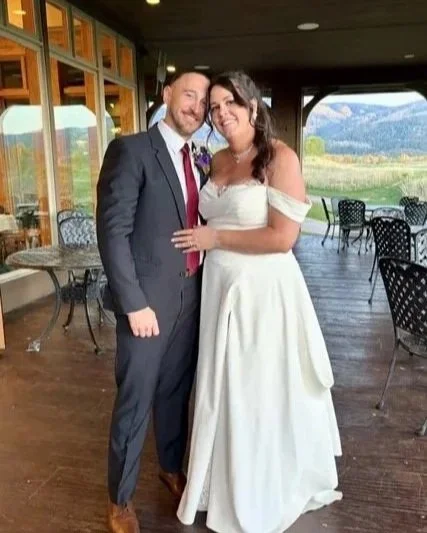 A bride and groom smiling and posing together at a wedding venue with outdoor scenery in the background.