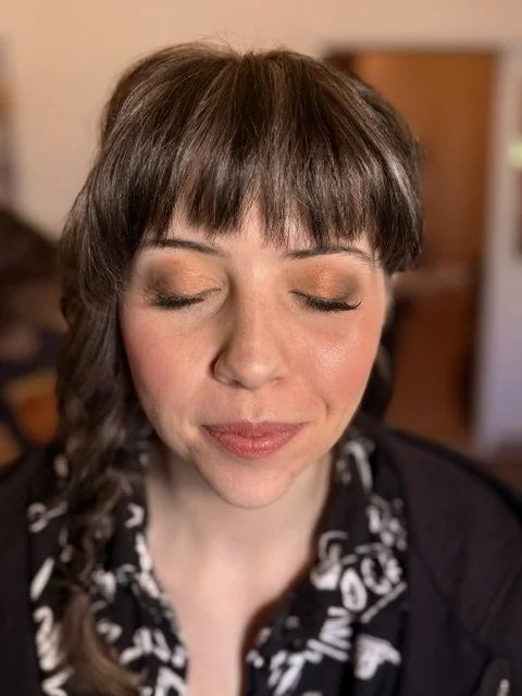 A woman with light skin and brown hair with bangs, eyes closed, smiling gently in a cozy indoor setting.