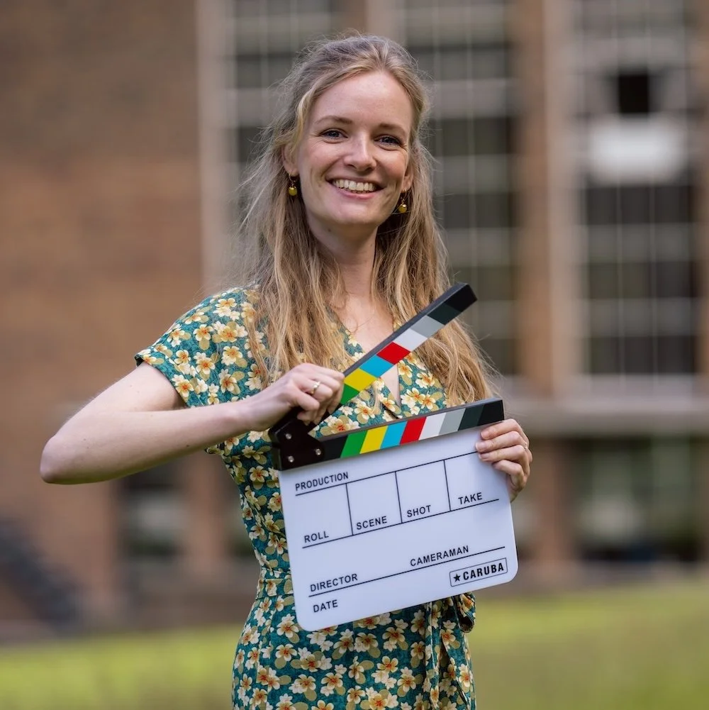 Een vrouw houdt een filmclapperboard vast en staat buiten voor een gebouw.