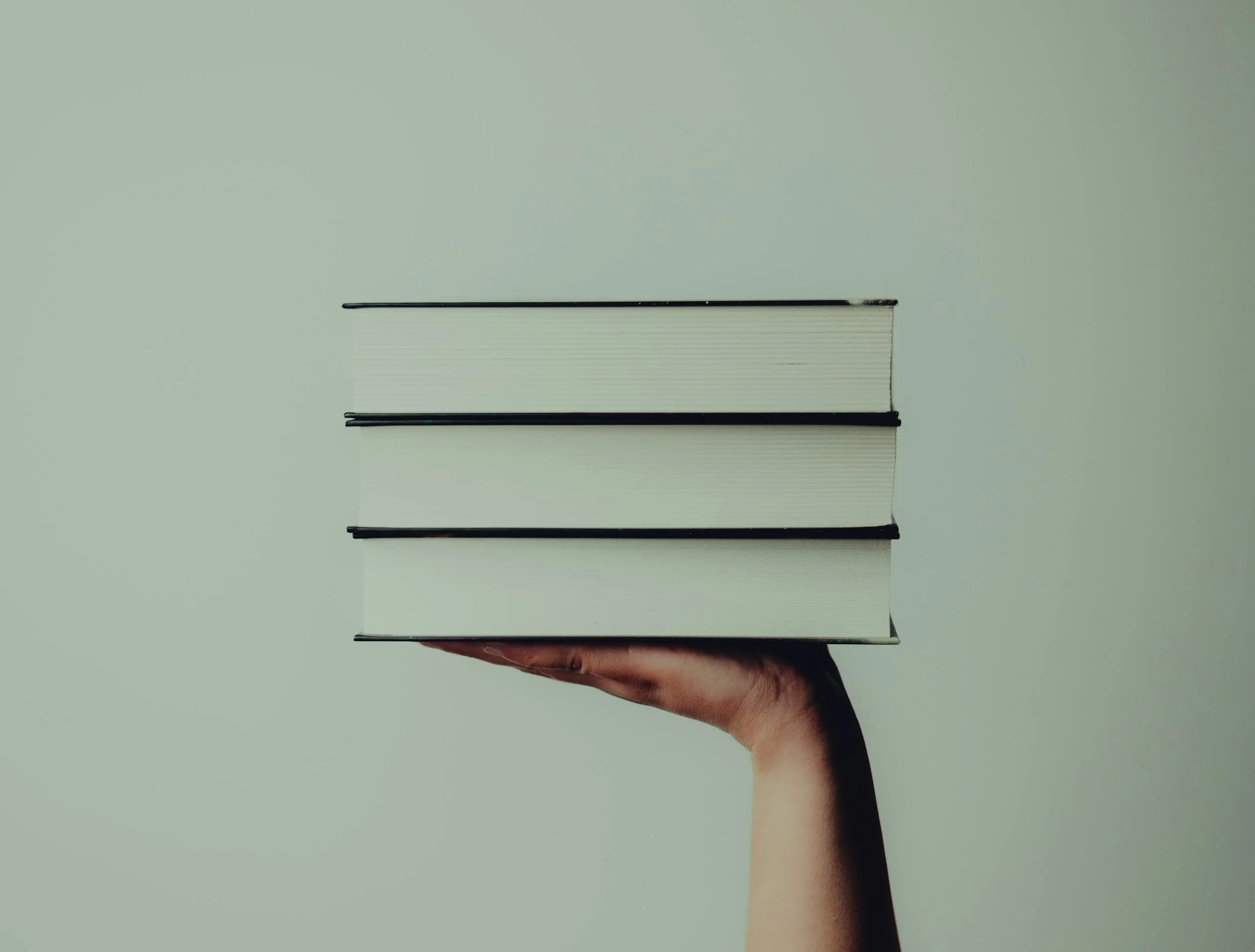 A hand holding a closed book against a plain background.