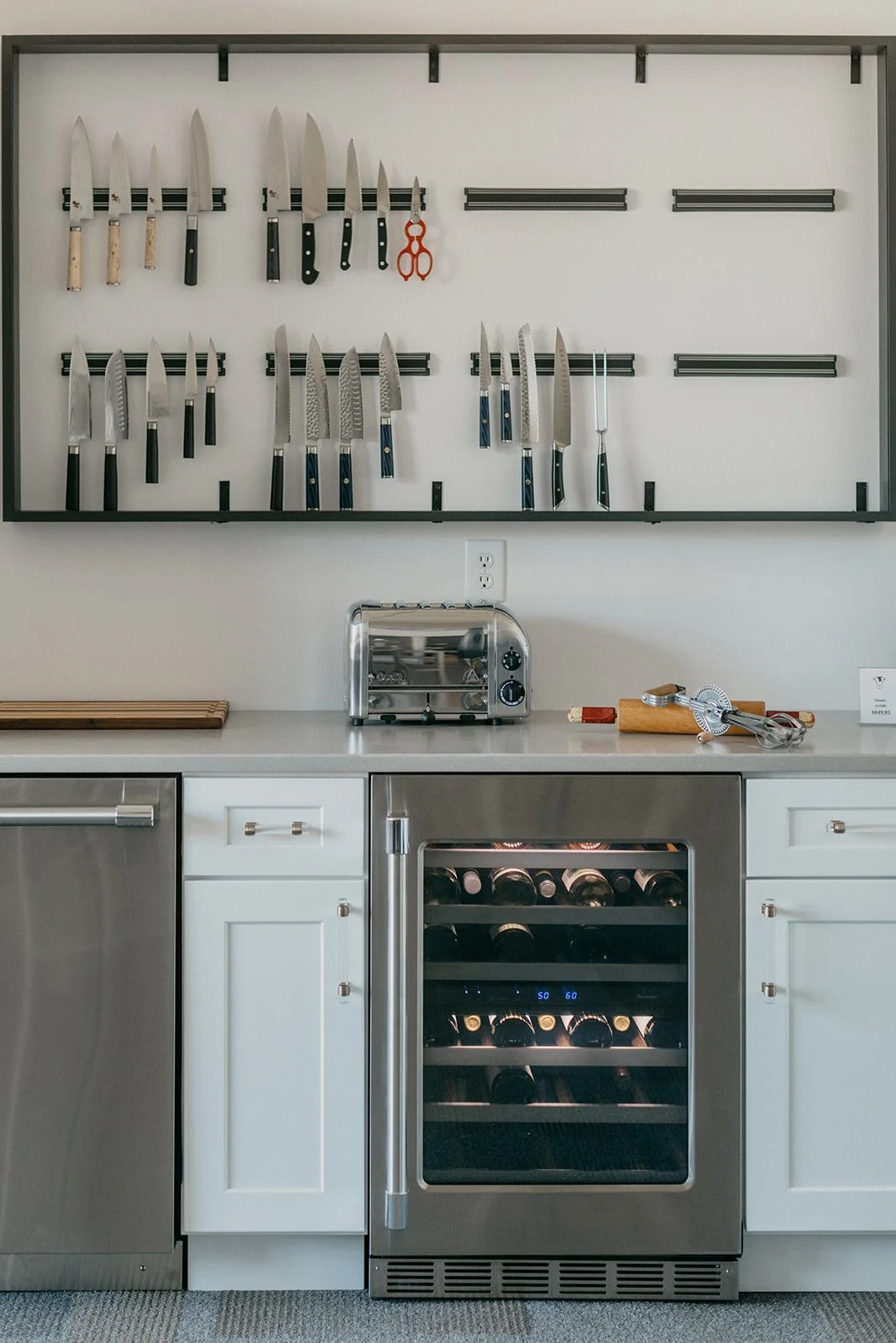 Kitchen with knife collection on a magnetic wall, toaster on the countertop, wine cooler with bottles, and white cabinets.