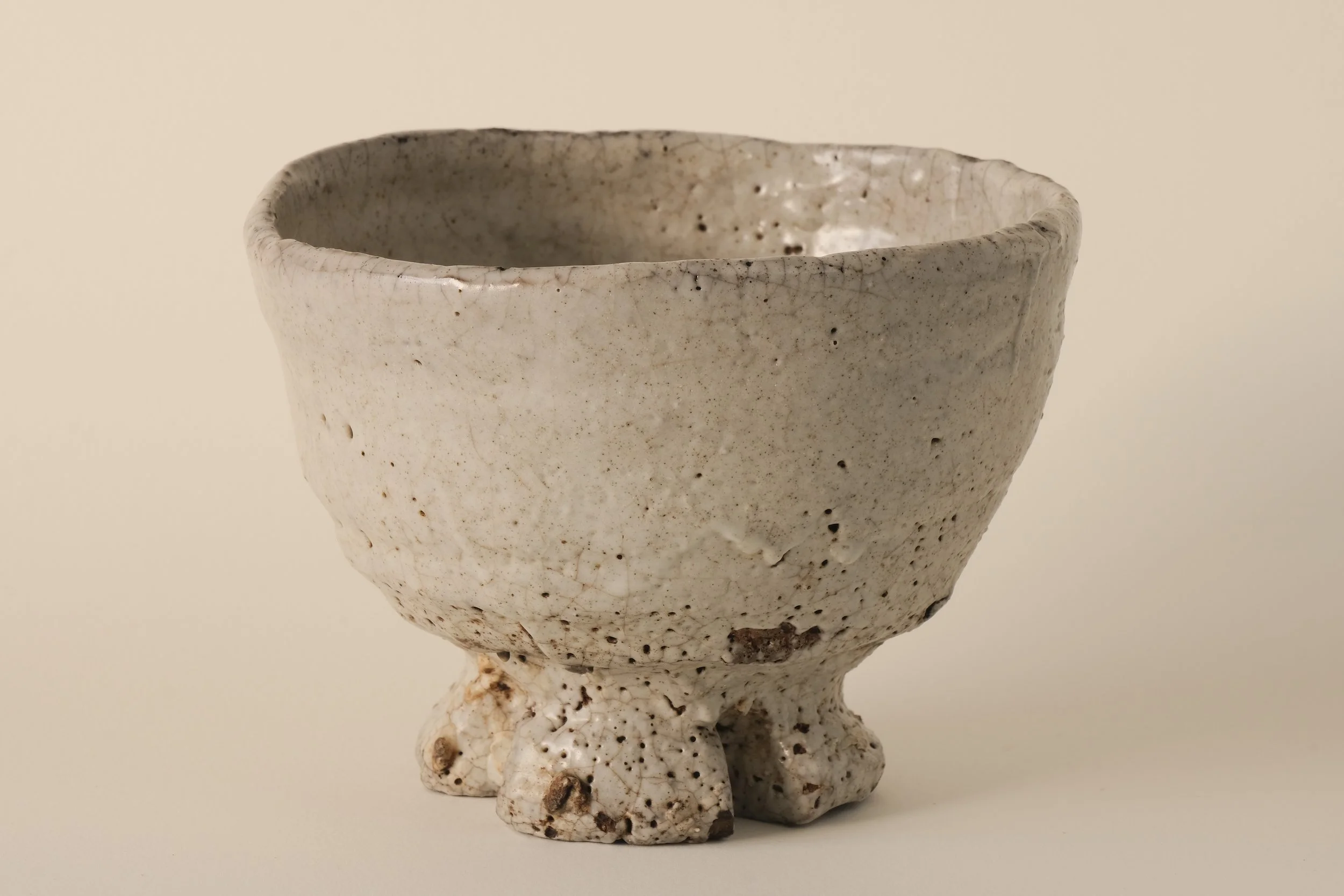 A ceramic bowl with three small legs, off-white in color with a speckled surface and rough texture.