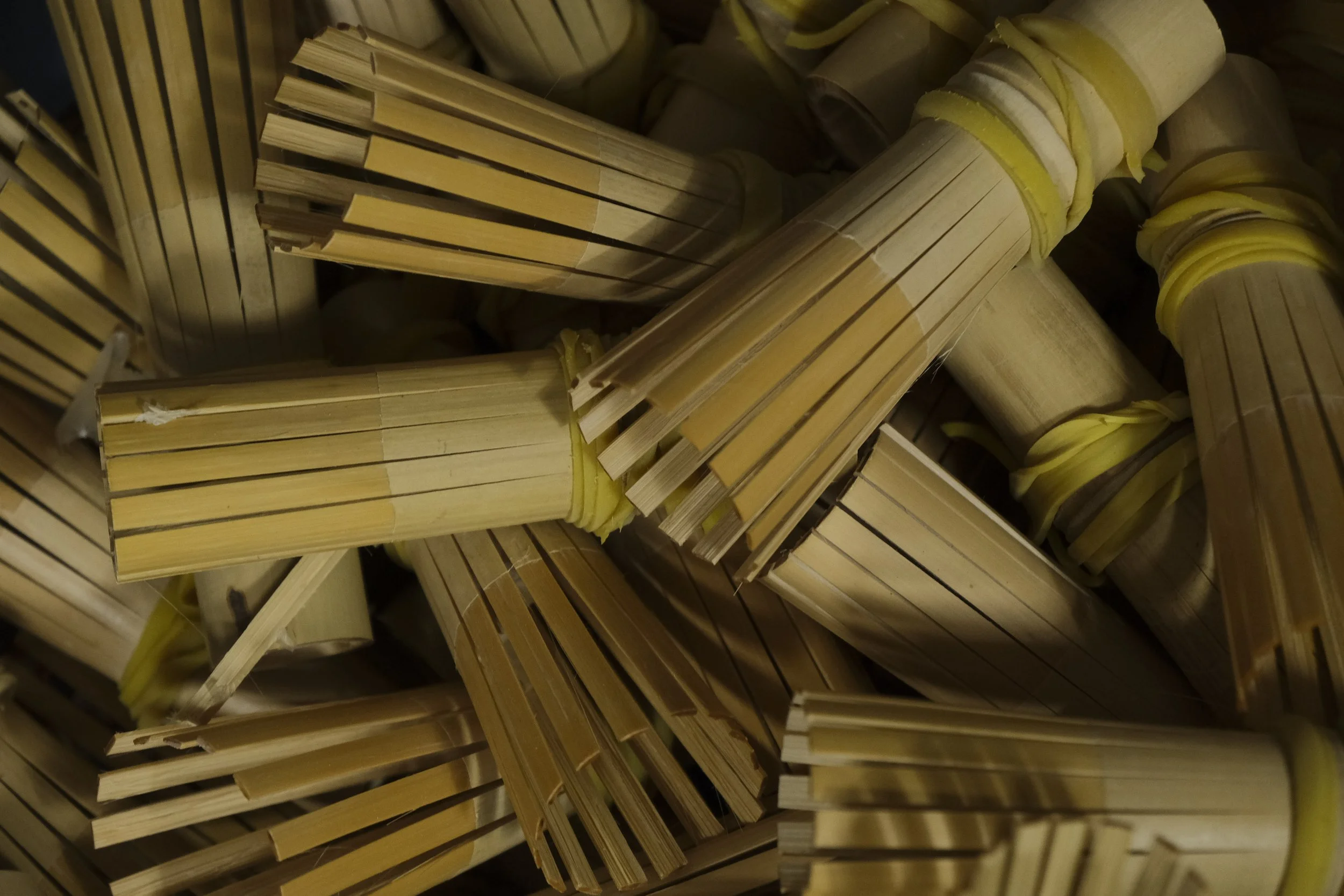A pile of disposable bamboo drink stirrers bundled with yellow rubber bands.