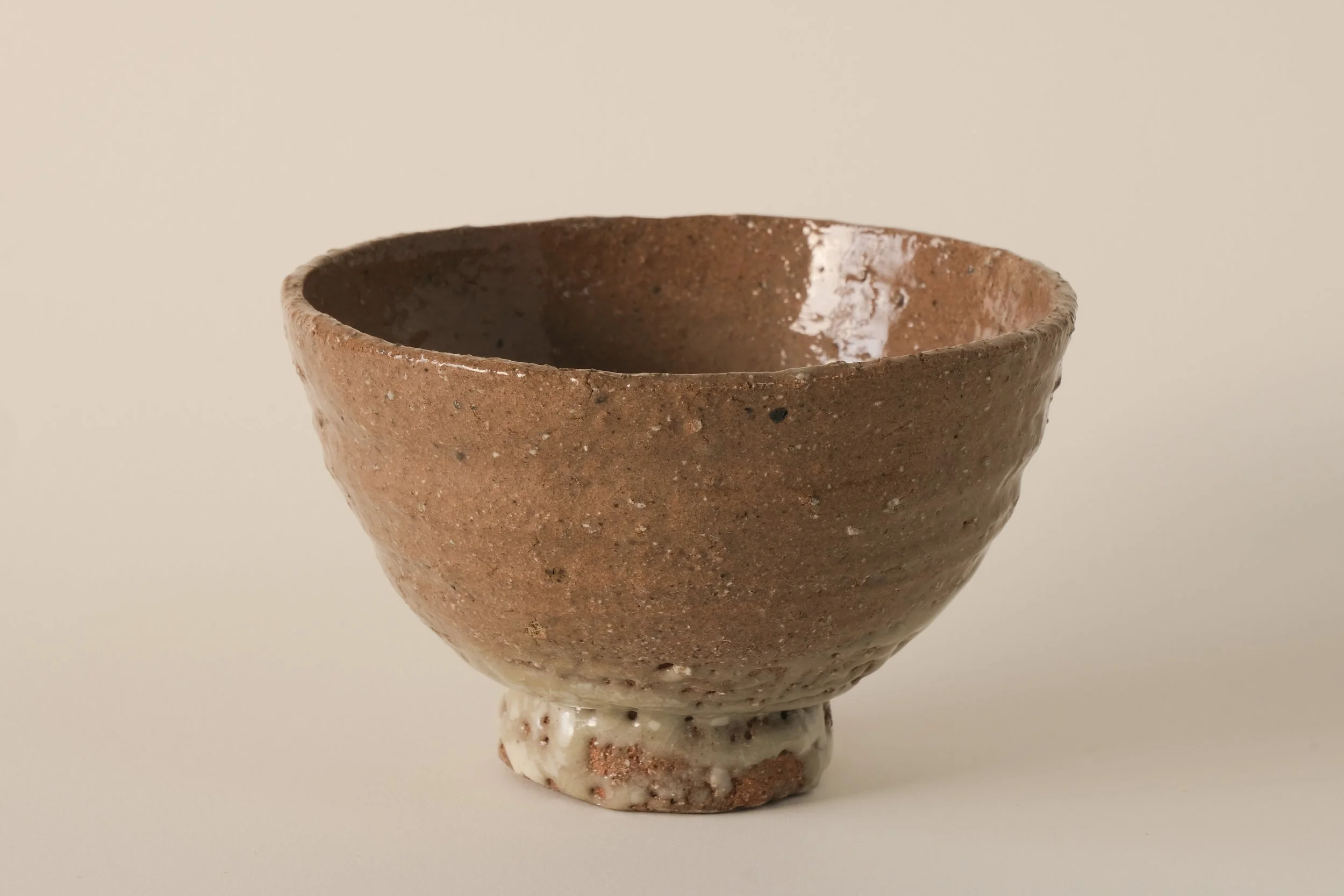 A handmade ceramic bowl with a rough, textured exterior and a smooth glazed interior, on a plain surface.