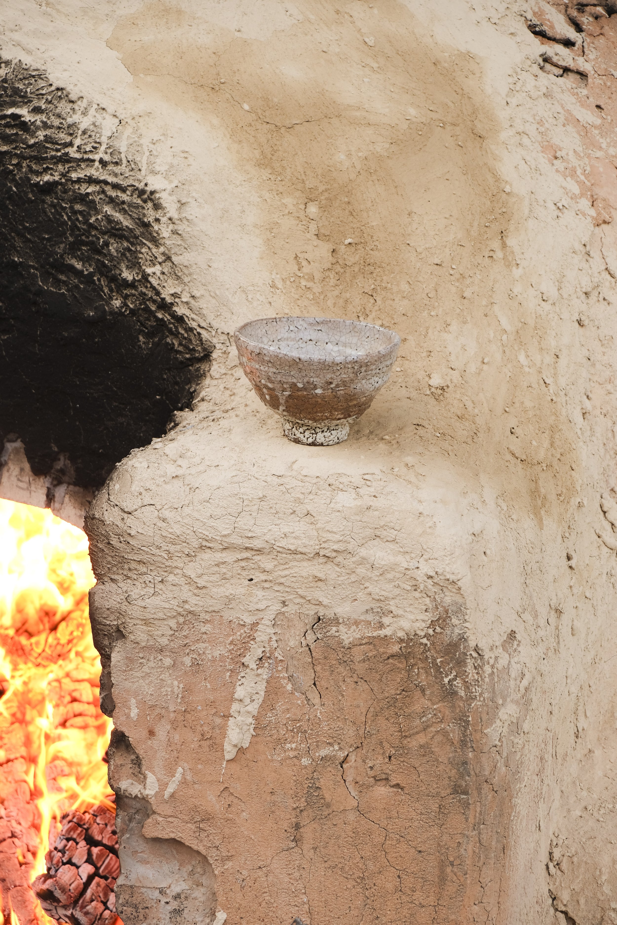 A rustic ceramic bowl resting on a rough, crumbling bricks wall next to an open fire.