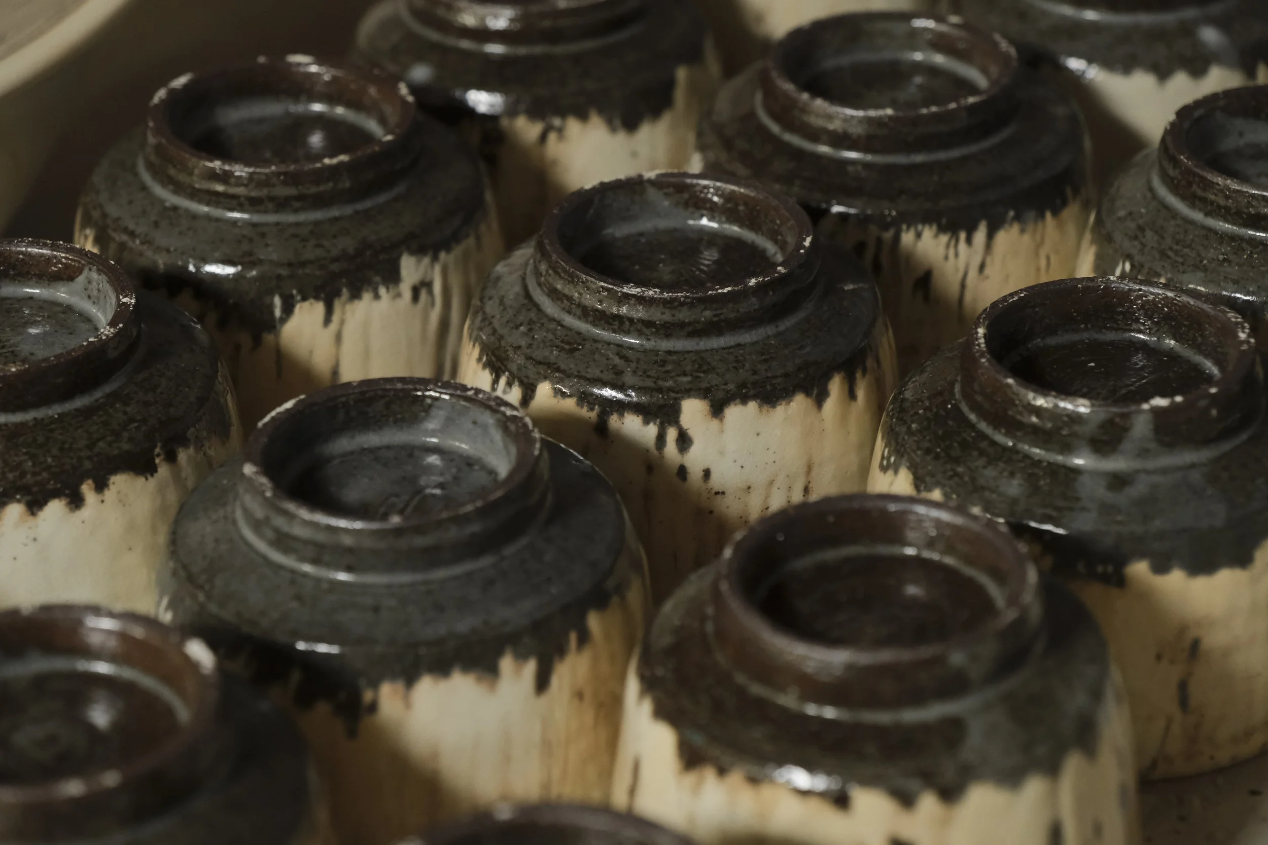 Close-up of upside-down ceramic cups with black glaze inside, arranged in a box or container.