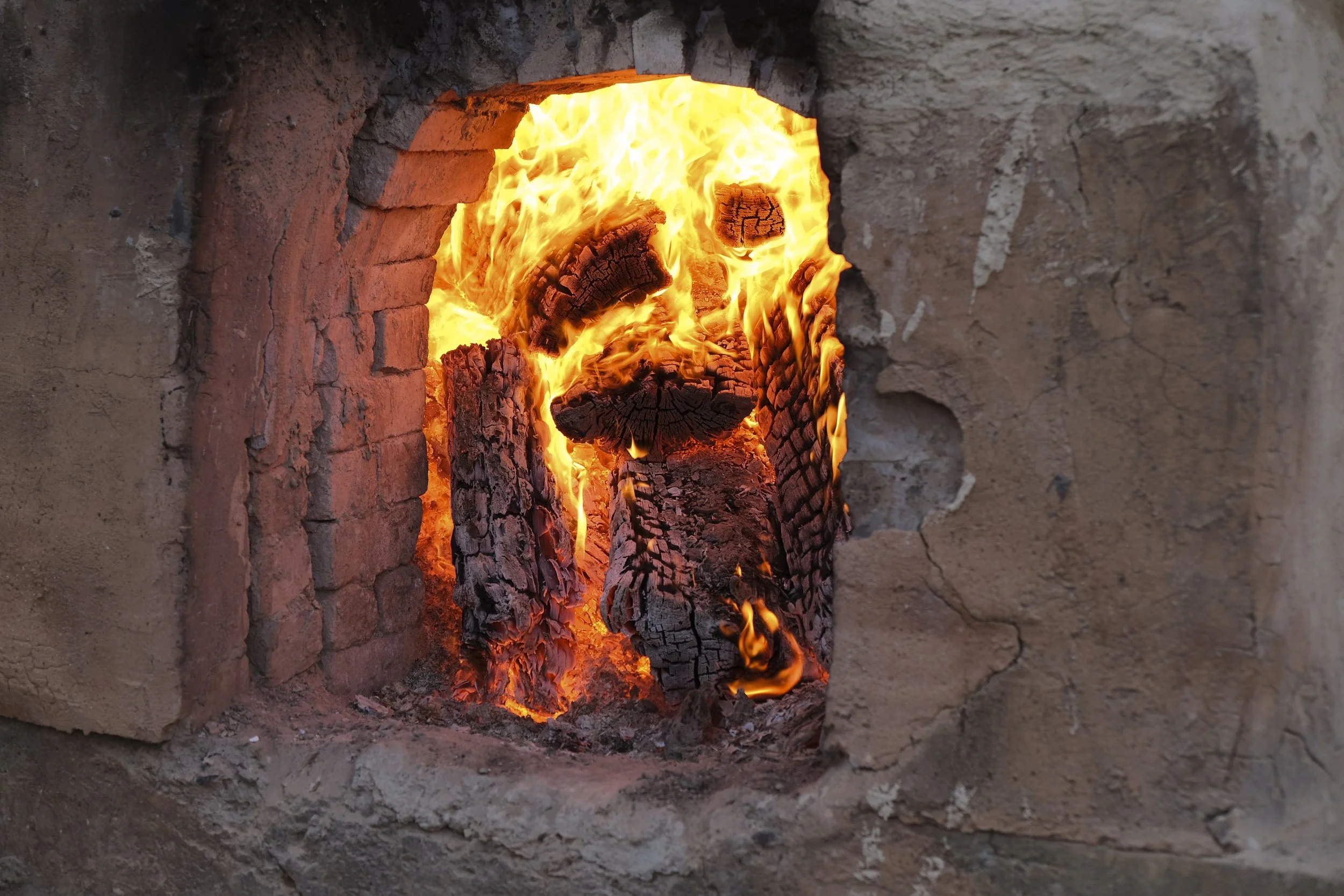 Fire burning inside a brick kiln with glowing wood logs.