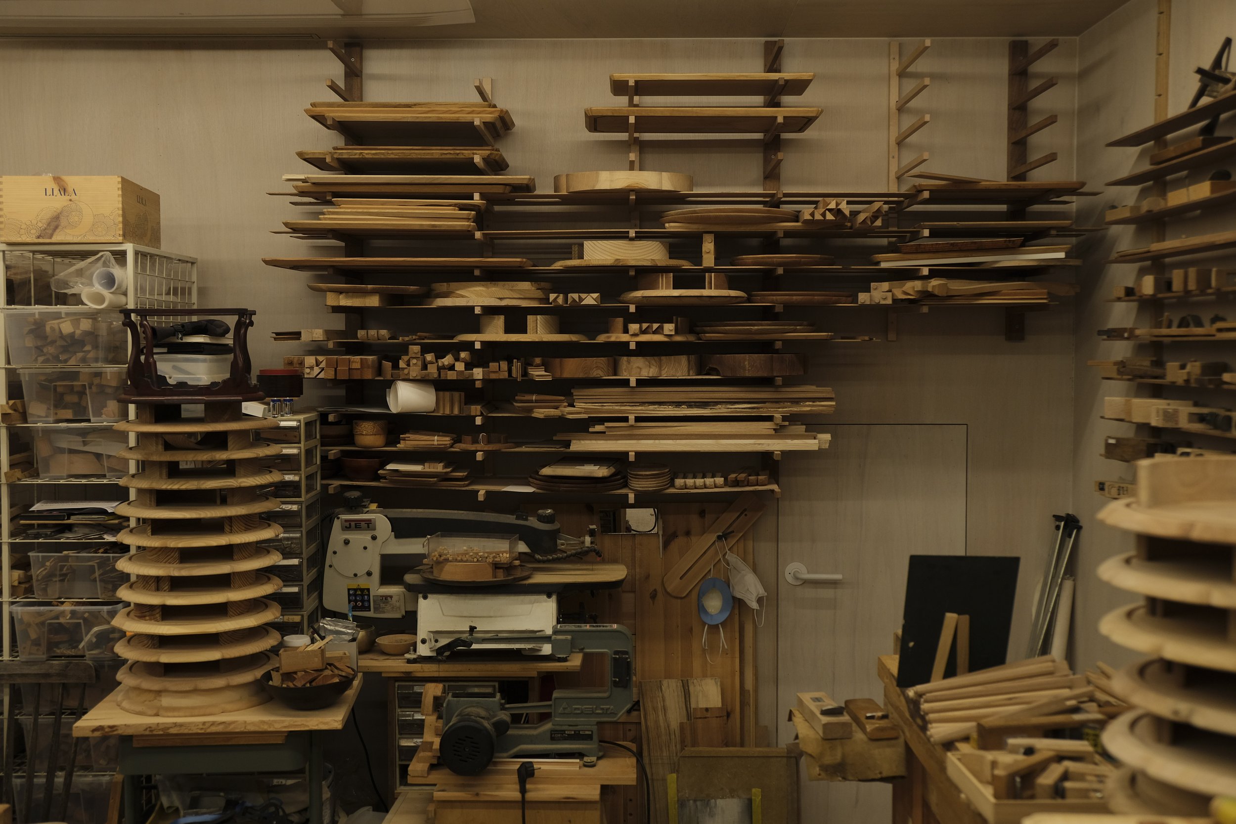 Woodworking workshop with shelves of various wooden boards, tools, and equipment.