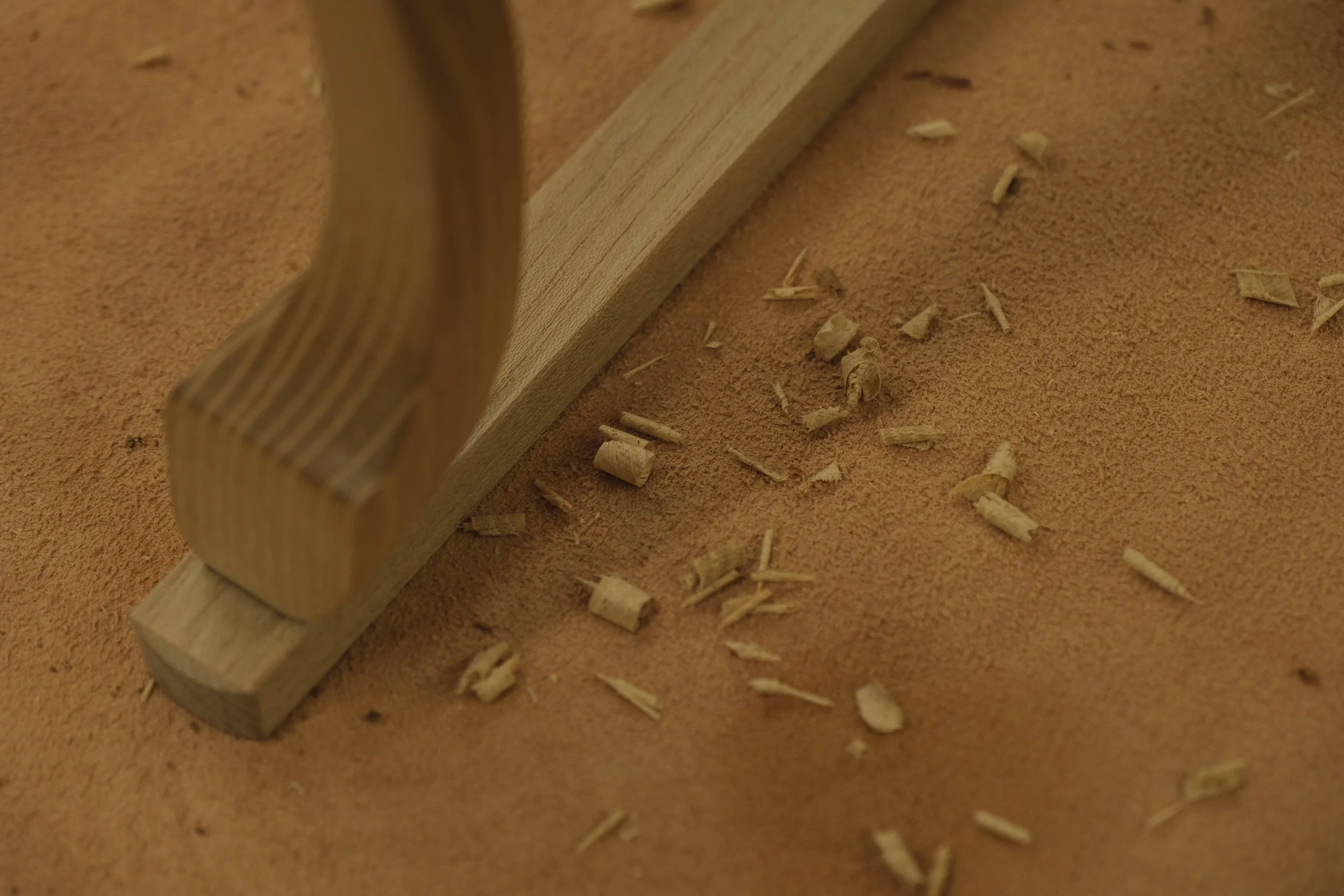 Close-up of a wooden furniture leg with wood shavings and debris on an orange surface.