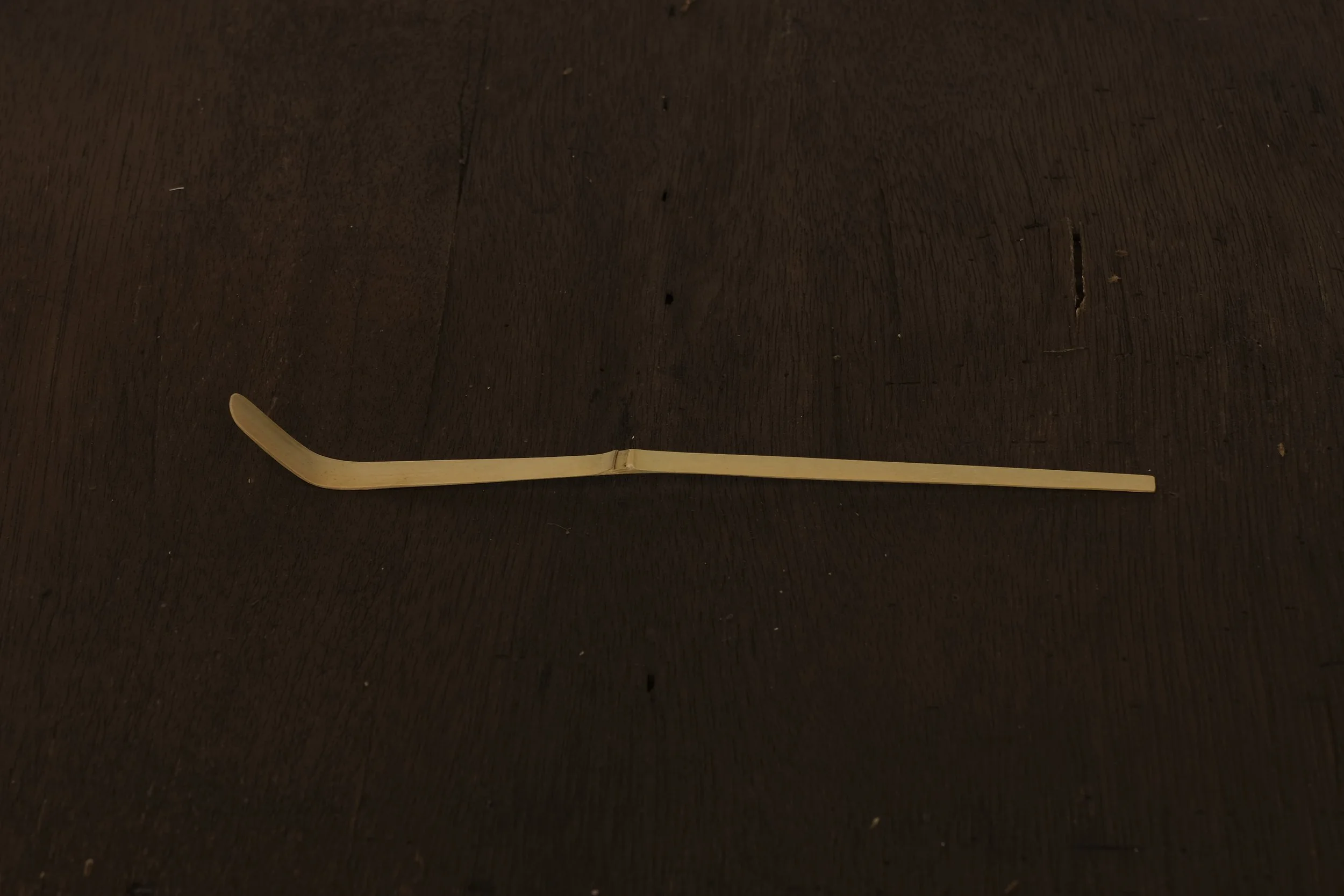 An eyebrow spoolie brush with a light wooden handle lying on a dark wooden surface.
