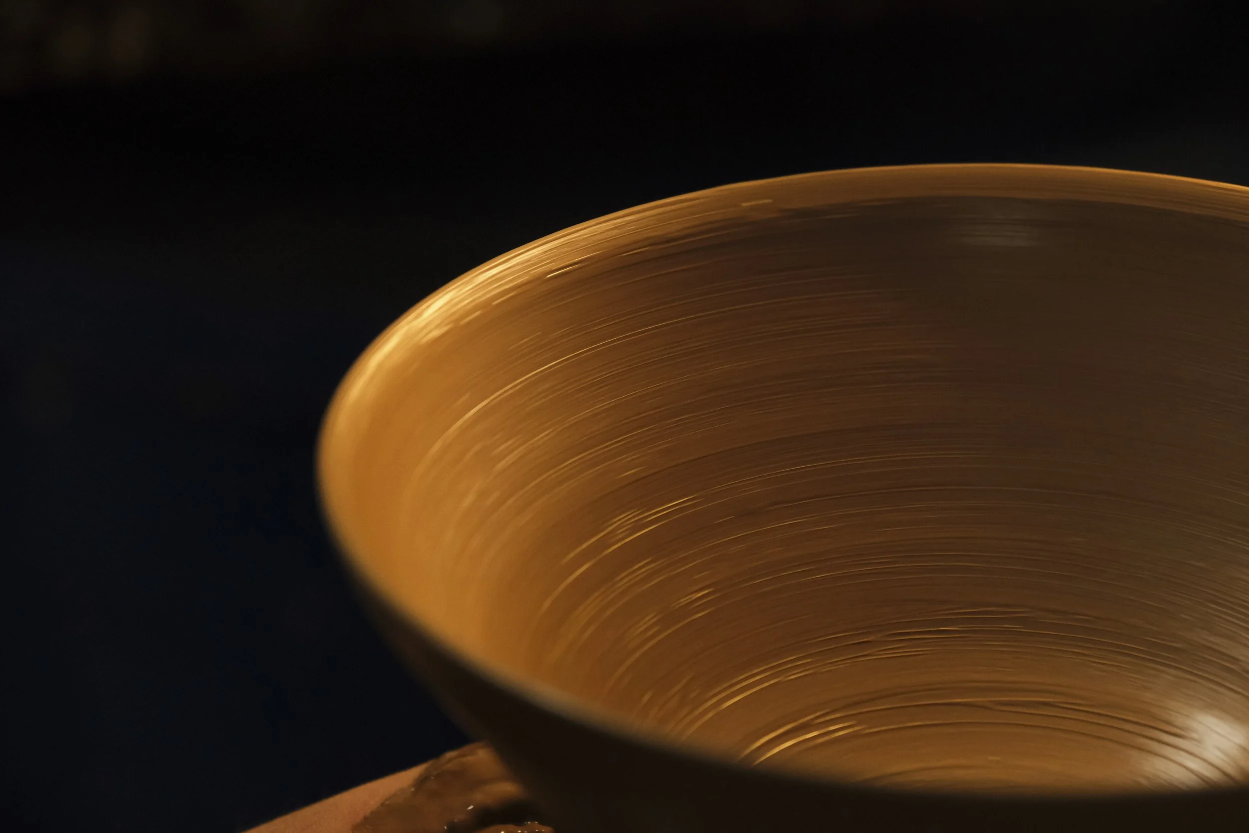 Close-up of a metallic copper bowl with visible concentric circular textures, set against a dark background.