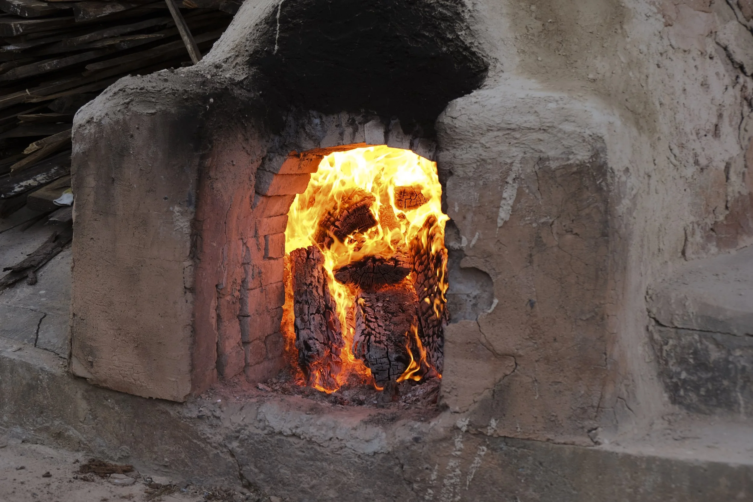Close-up of a traditional brick oven with fire burning inside, surrounded by a rustic stone and clay structure.