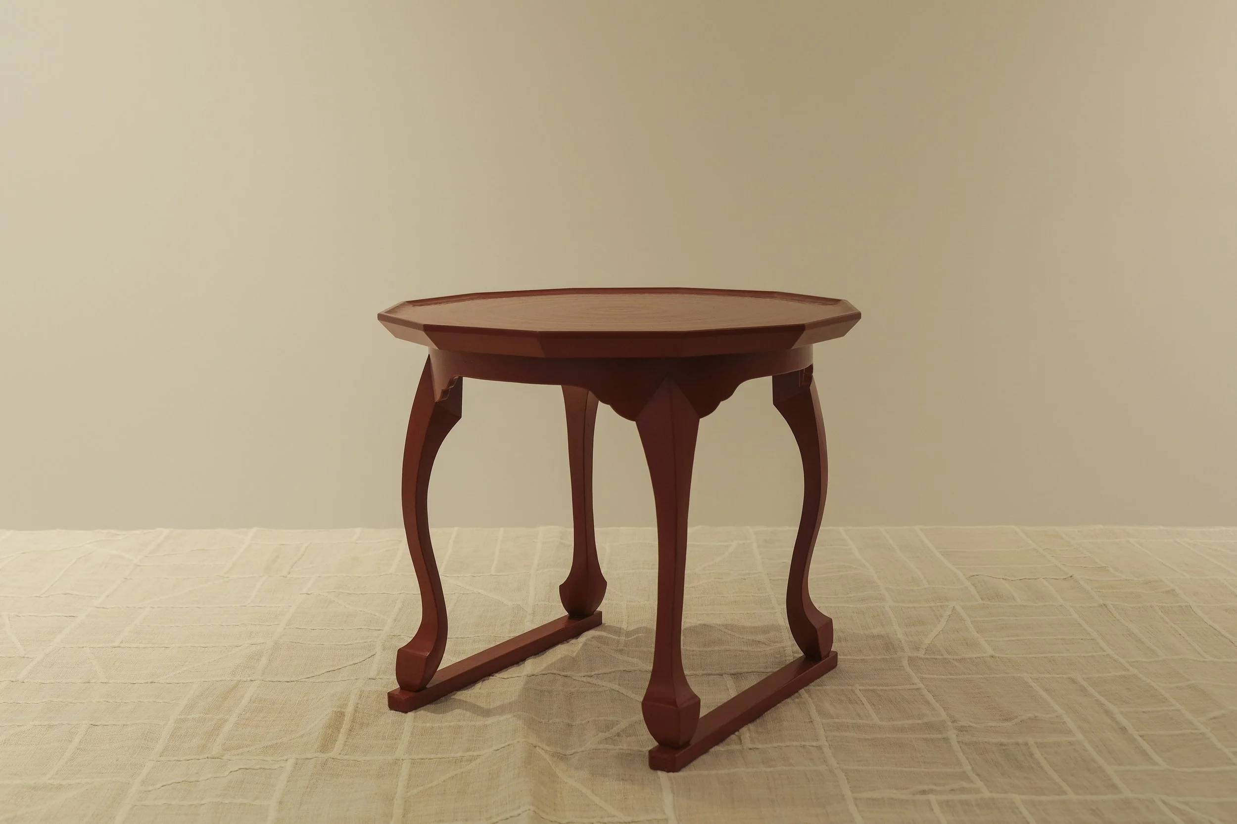 A small wooden table with curved legs on a beige tablecloth against a plain wall.