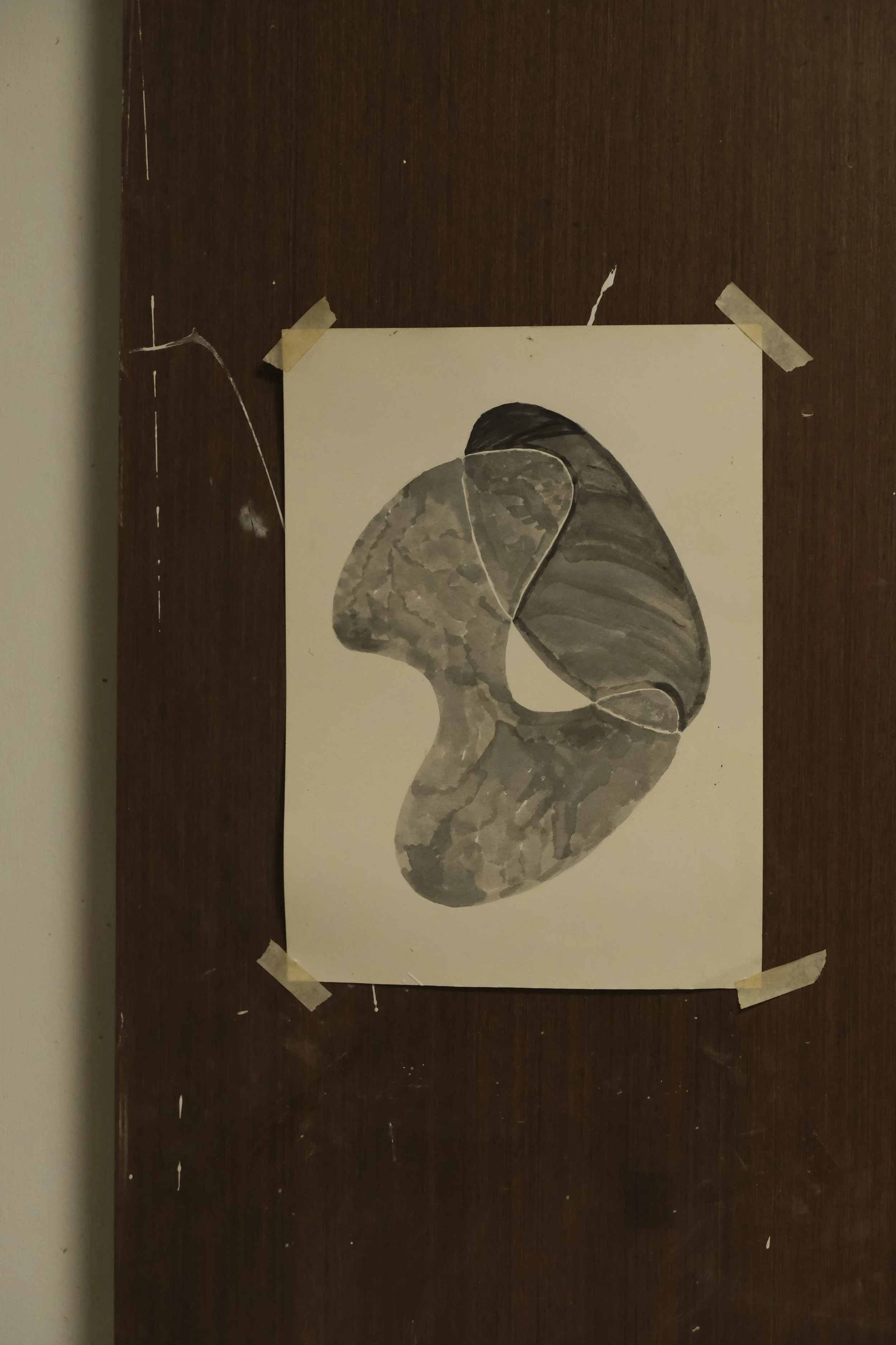 A monochrome abstract watercolor painting of a human face in profile, taped to a dark wooden surface.