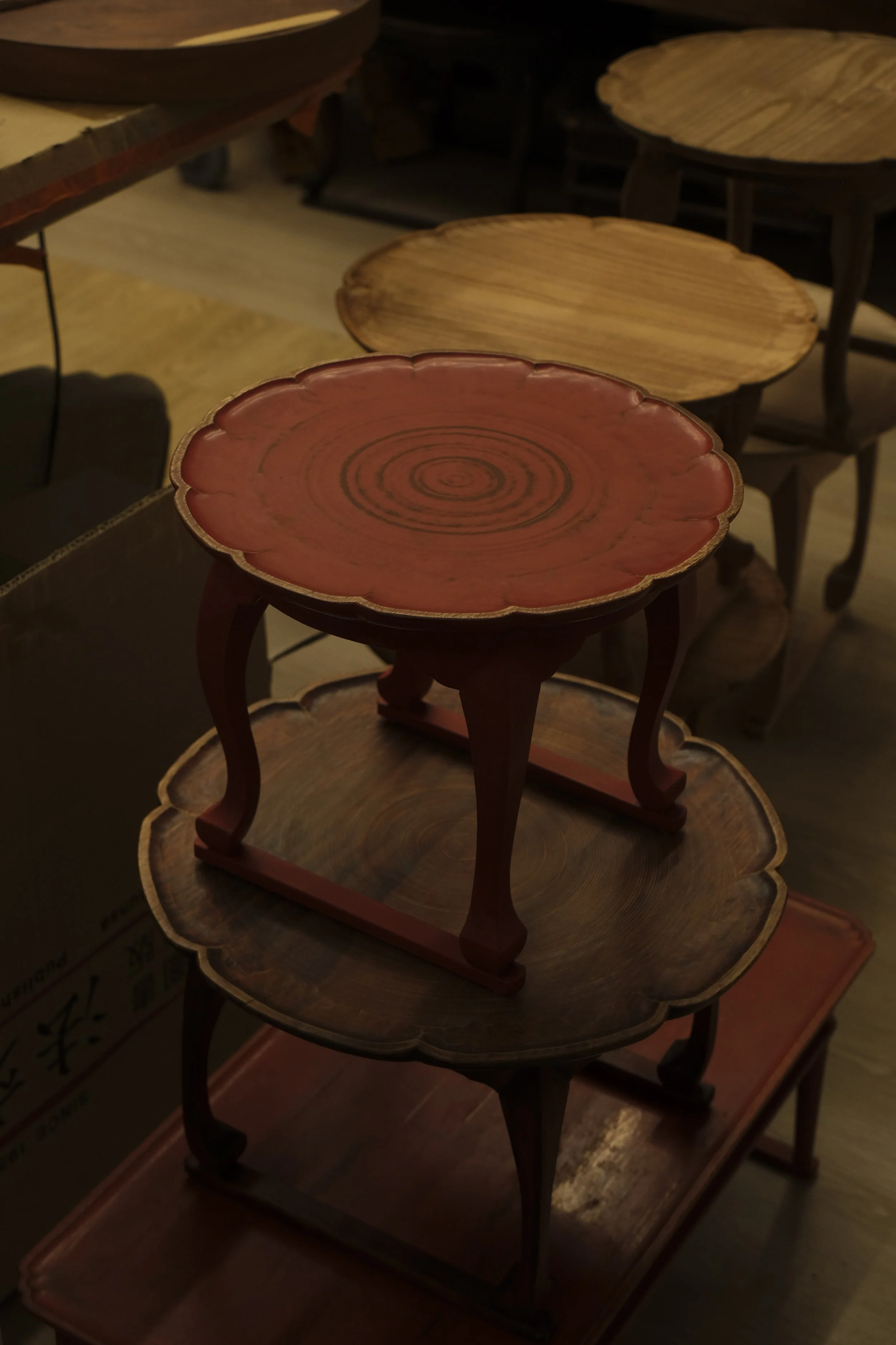 Stacked small wooden tables in a store with a dark and warm ambiance.