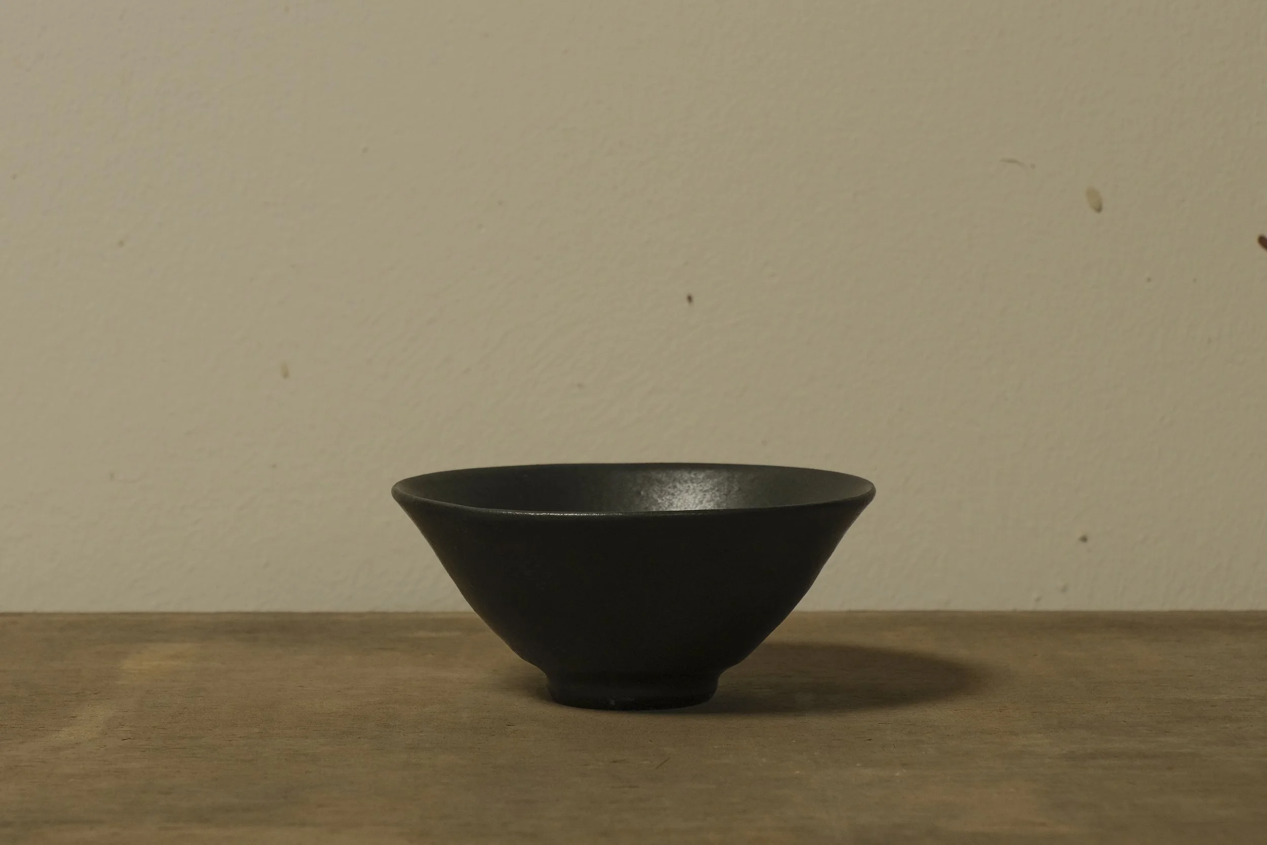 A black ceramic bowl placed on a wooden surface against a plain wall.